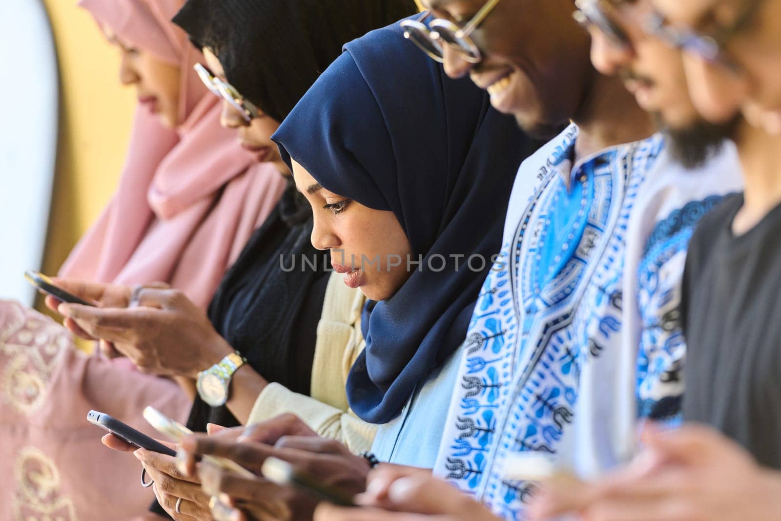 A diverse group of teenagers standing together against a wall, engrossed in their smartphones, showcasing modern connectivity and social interaction.