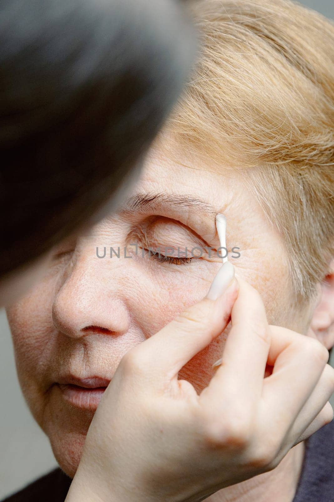 A cosmetologist paints the eyebrows of an elderly woman. by Nataliya