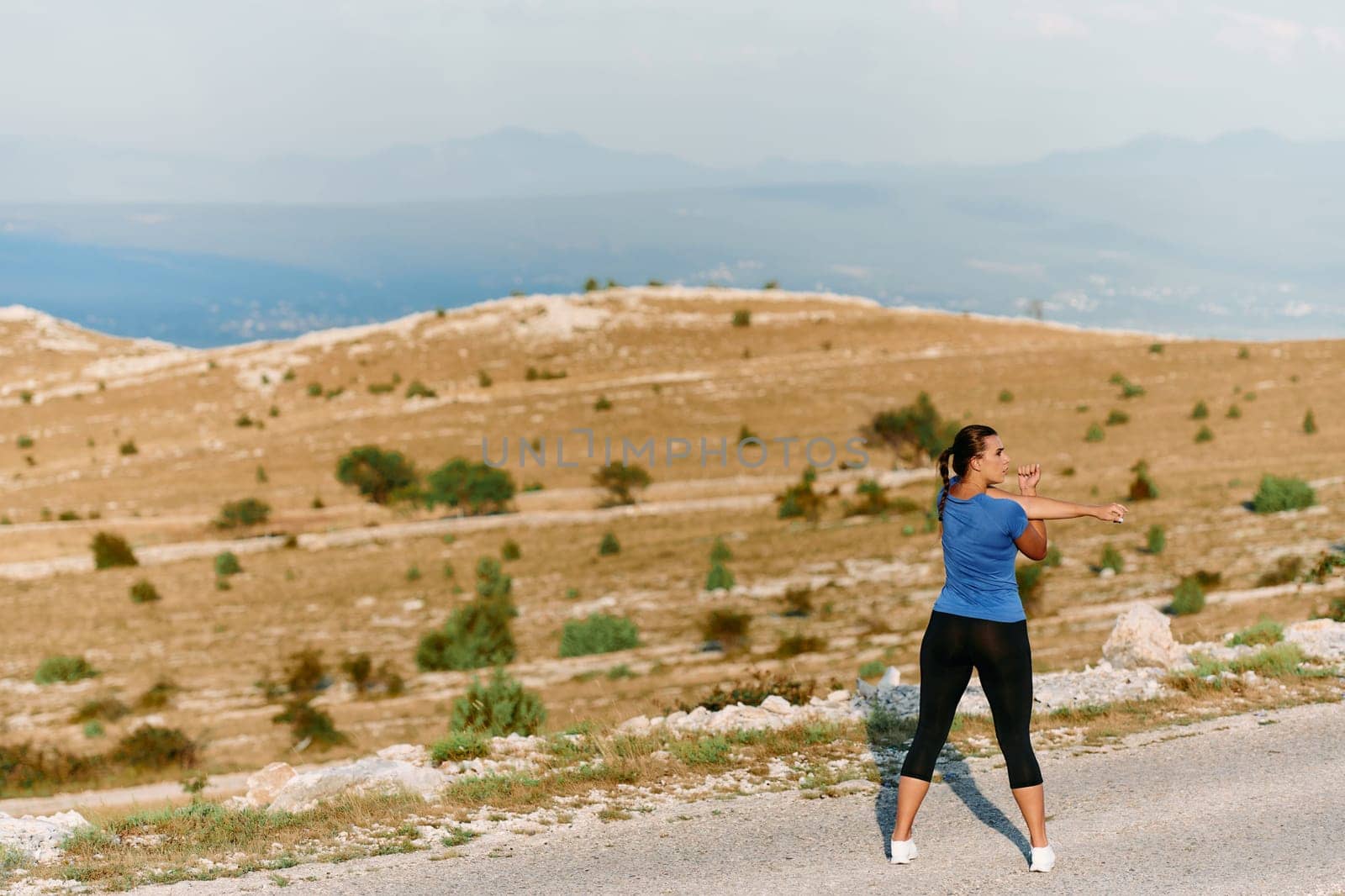 A determined female athlete stretches her muscles after a strenuous run through rugged mountain terrain, surrounded by breathtaking rocky landscapes.