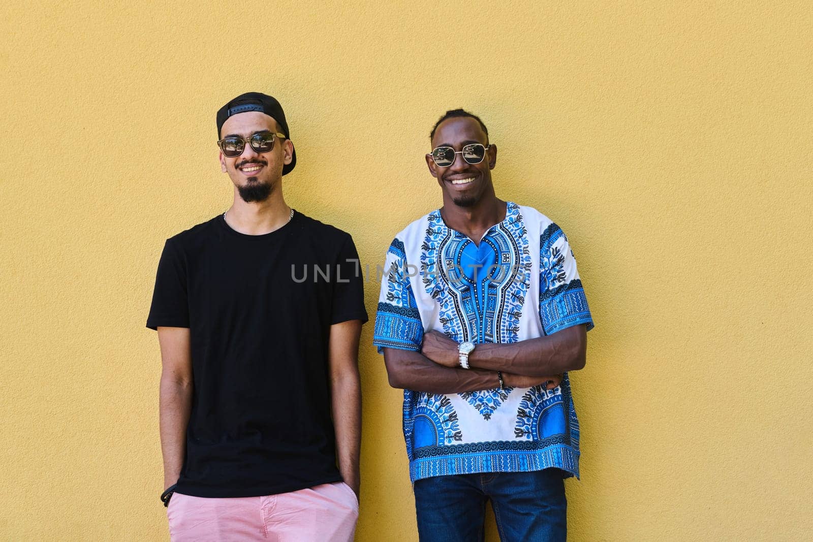 Two Male Friends: African American Teenager in Sudanese Traditional Attire Leaning Against Yellow Wall by dotshock