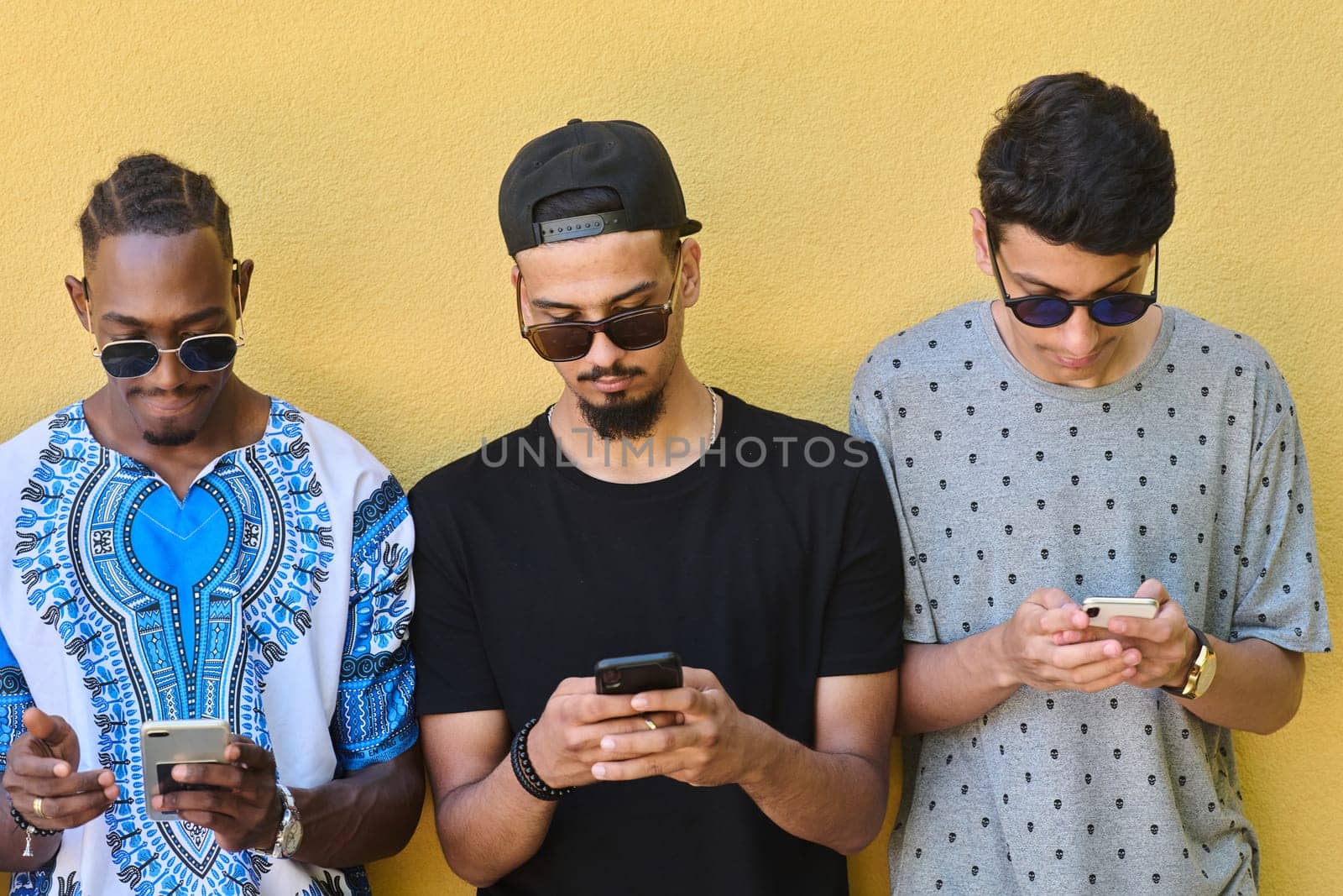 A diverse group of teenagers standing together against a wall, engrossed in their smartphones, showcasing modern connectivity and social interaction.
