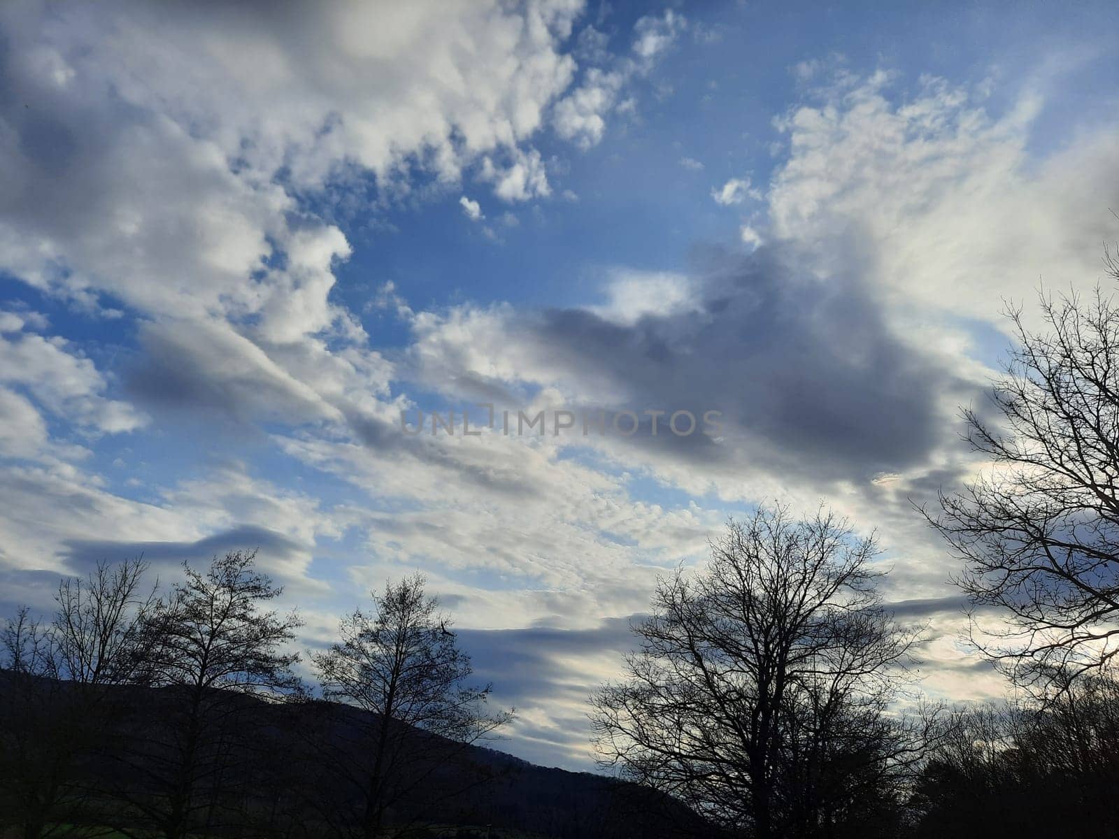 Some gray-white clouds in the sky. The streaks of clouds are diffuse and reflect beautiful sunlight in the blue sky at sunset. High quality photo