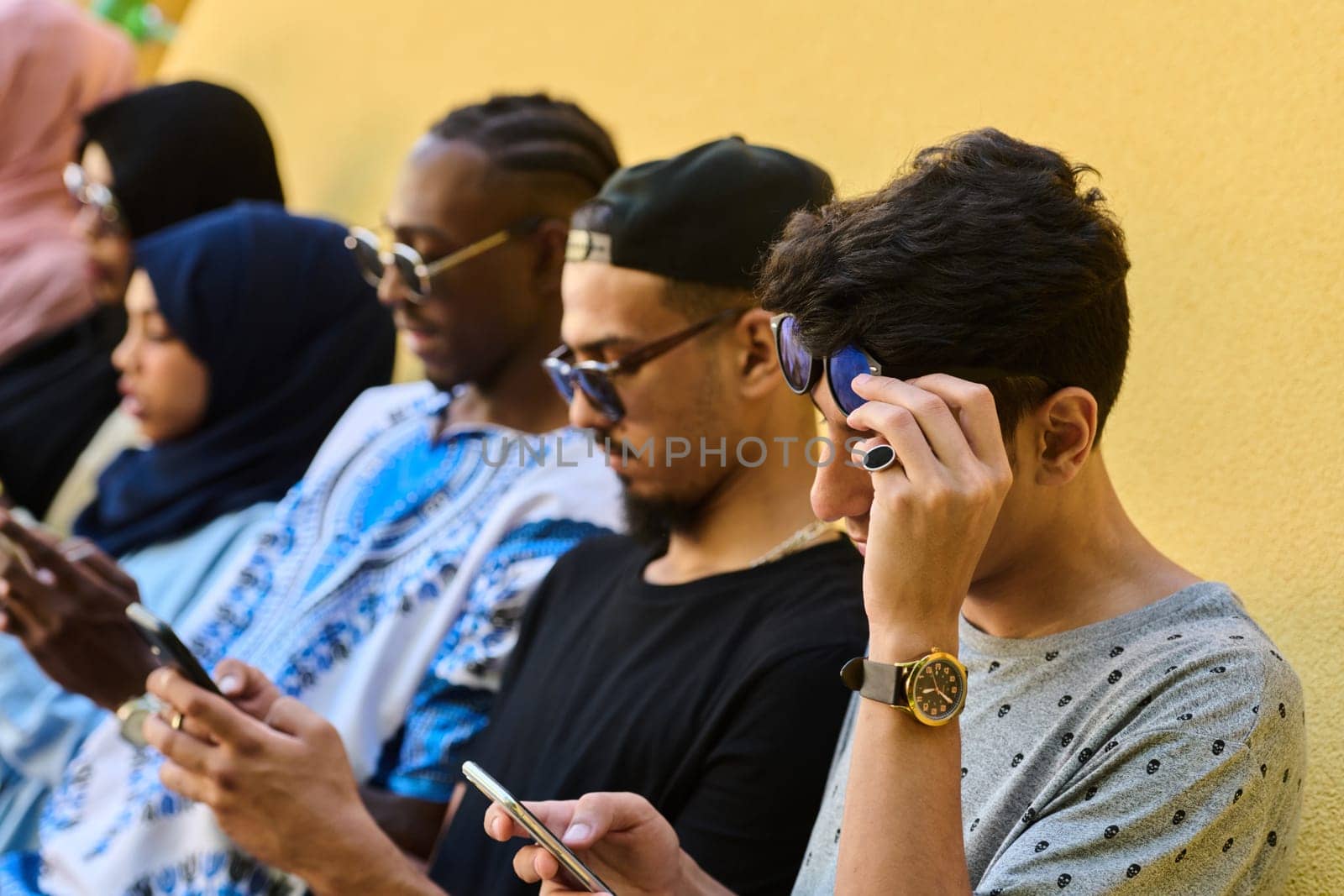 A diverse group of teenagers standing together against a wall, engrossed in their smartphones, showcasing modern connectivity and social interaction.