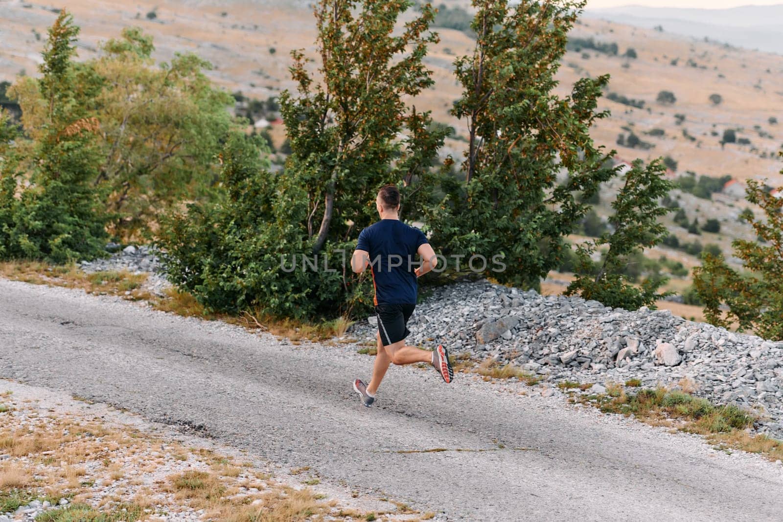 A muscular male athlete runs along a rugged mountain path at sunrise, surrounded by breathtaking rocky landscapes and natural beauty.