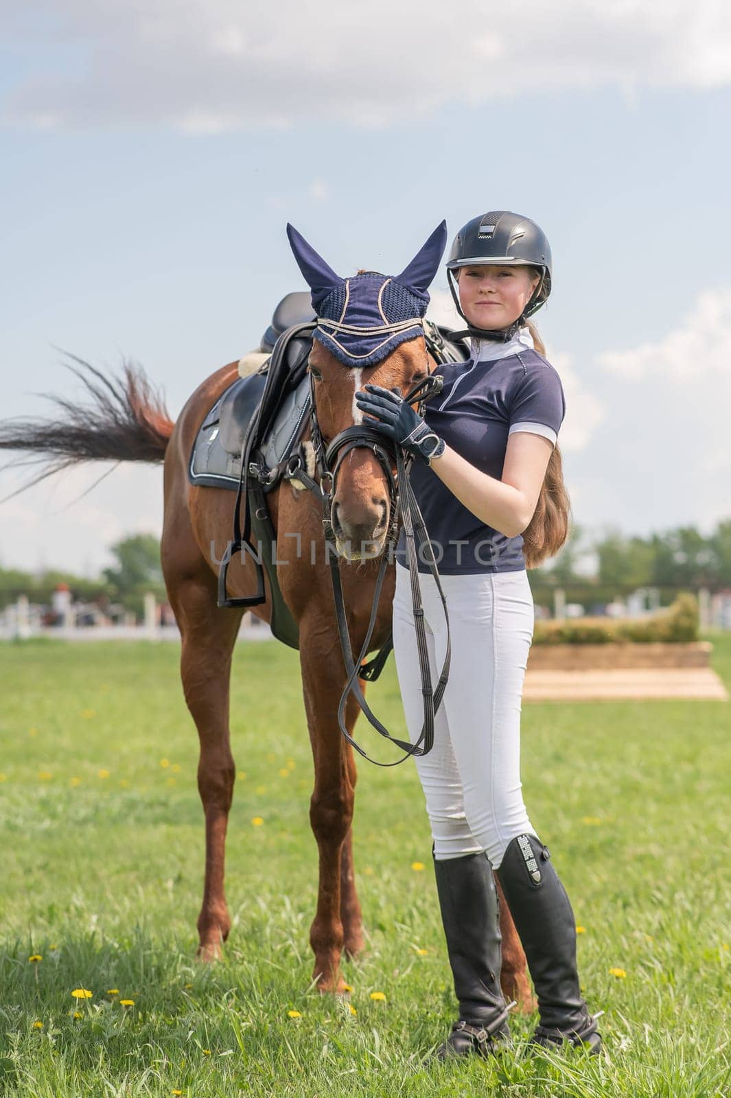 A young girl stands next to a horse before an equestrian competition. Vertical photo