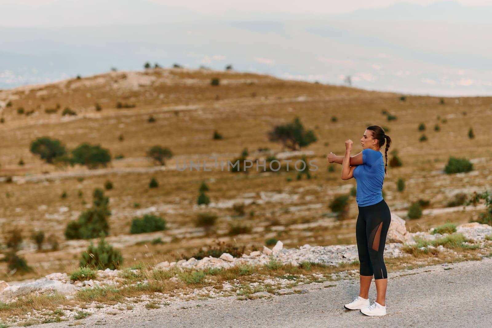 A determined female athlete stretches her muscles after a strenuous run through rugged mountain terrain, surrounded by breathtaking rocky landscapes.