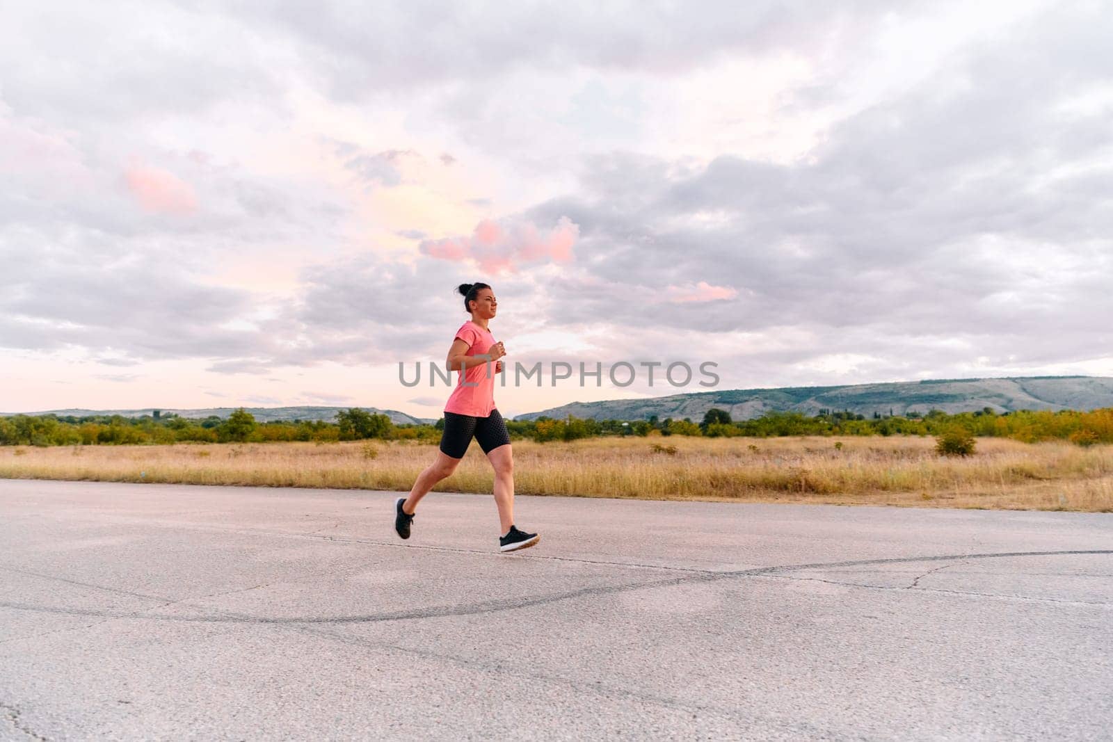 A determined athlete runs confidently under the sun, surrounded by stunning natural scenery, showcasing strength and resilience in her pursuit of fitness