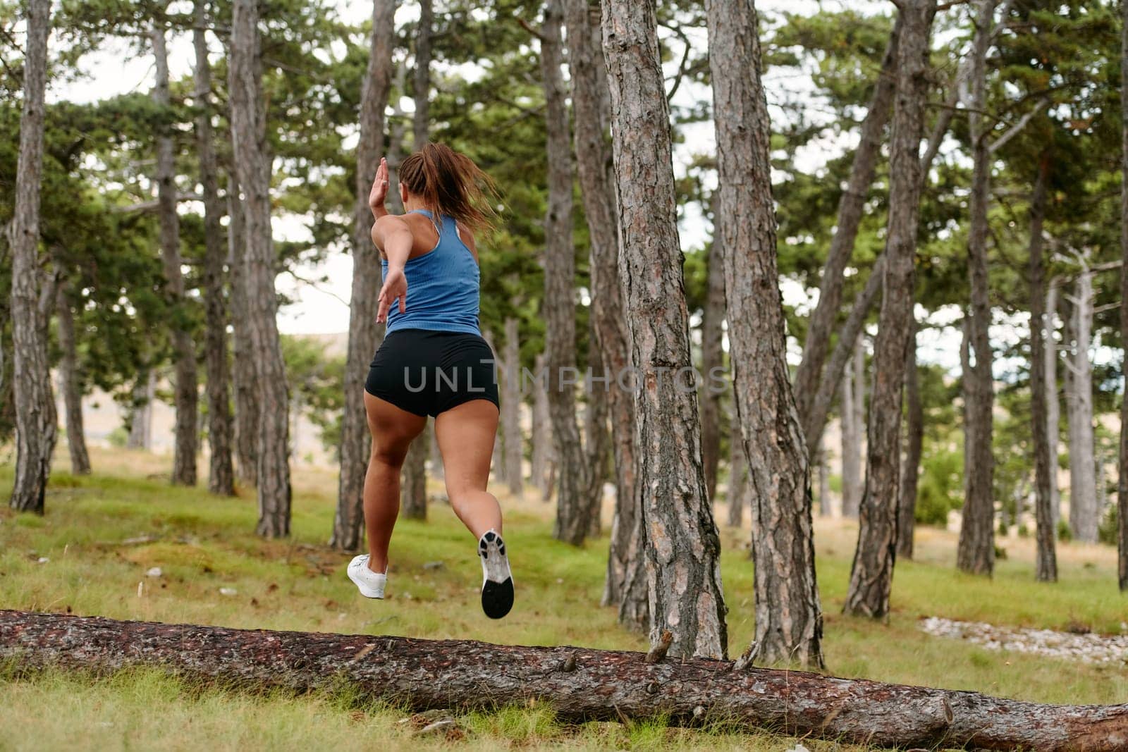 An intrepid woman fearlessly navigates through perilous forest terrain, effortlessly leaping over wooden obstacles with determination and grace, showcasing her adventurous spirit and athletic prowess