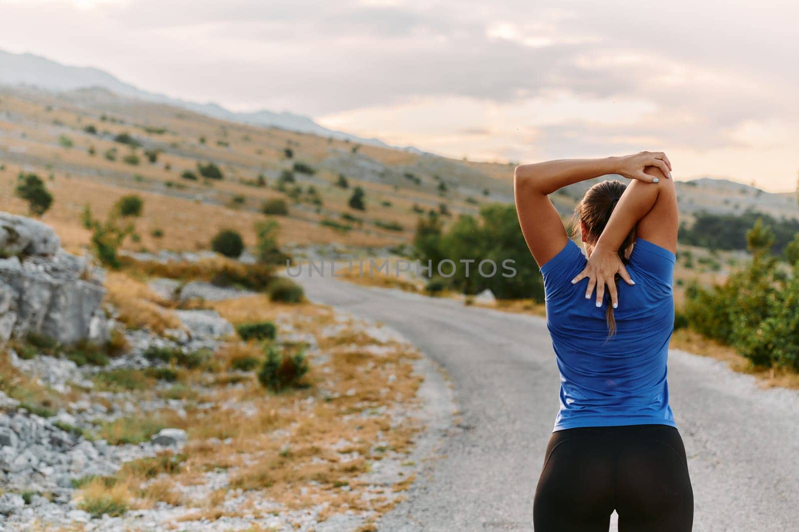 A determined female athlete stretches her muscles after a strenuous run through rugged mountain terrain, surrounded by breathtaking rocky landscapes.