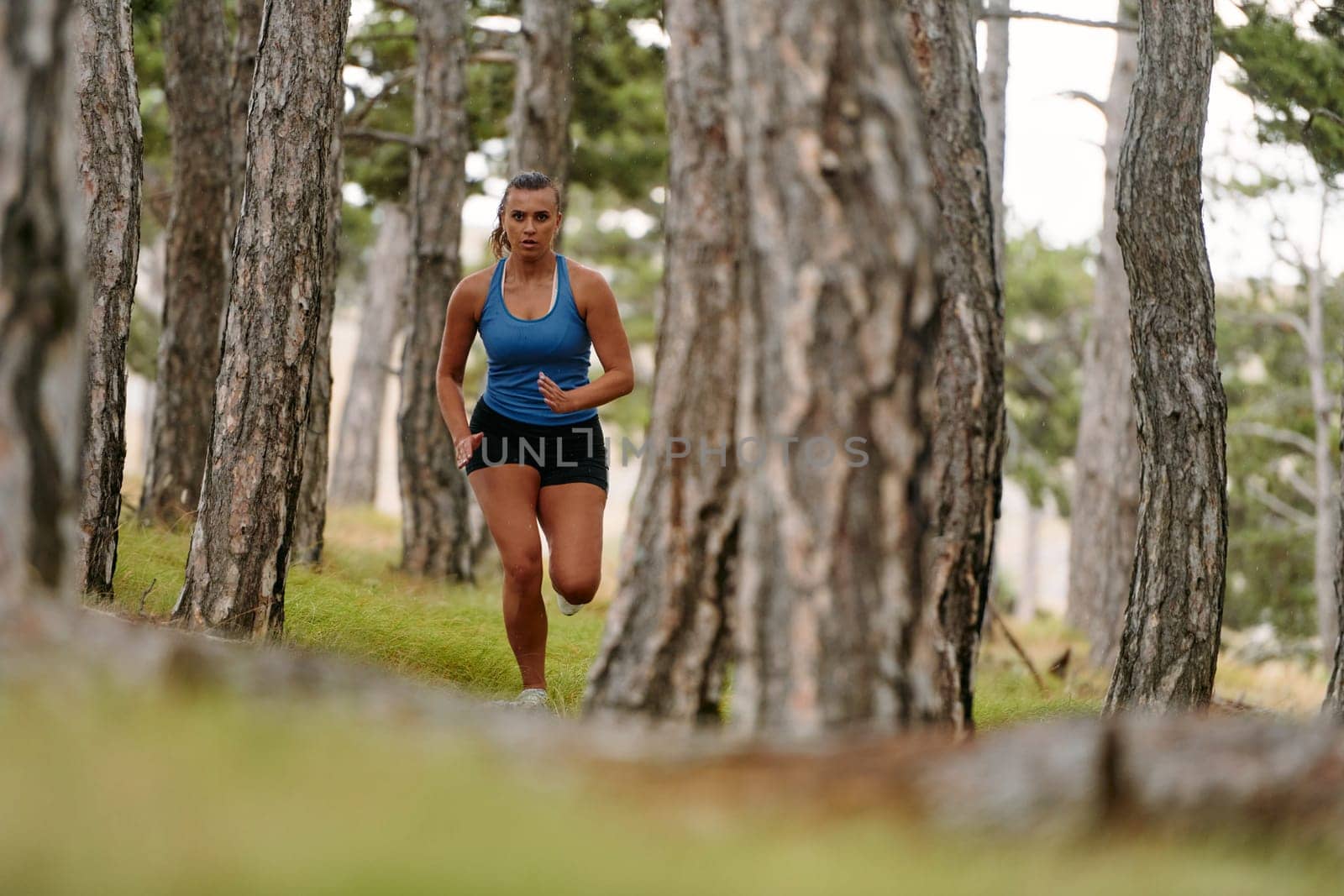 An intrepid woman fearlessly navigates through perilous forest terrain, effortlessly leaping over wooden obstacles with determination and grace, showcasing her adventurous spirit and athletic prowess