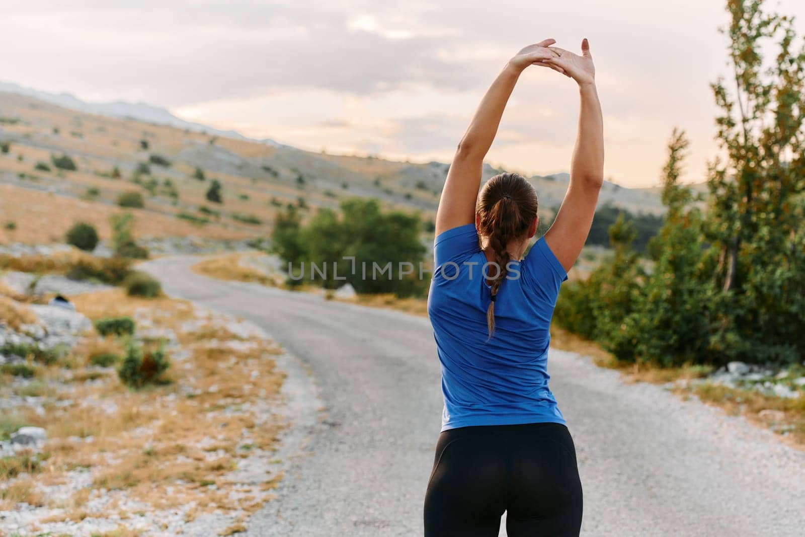 A determined female athlete stretches her muscles after a strenuous run through rugged mountain terrain, surrounded by breathtaking rocky landscapes.