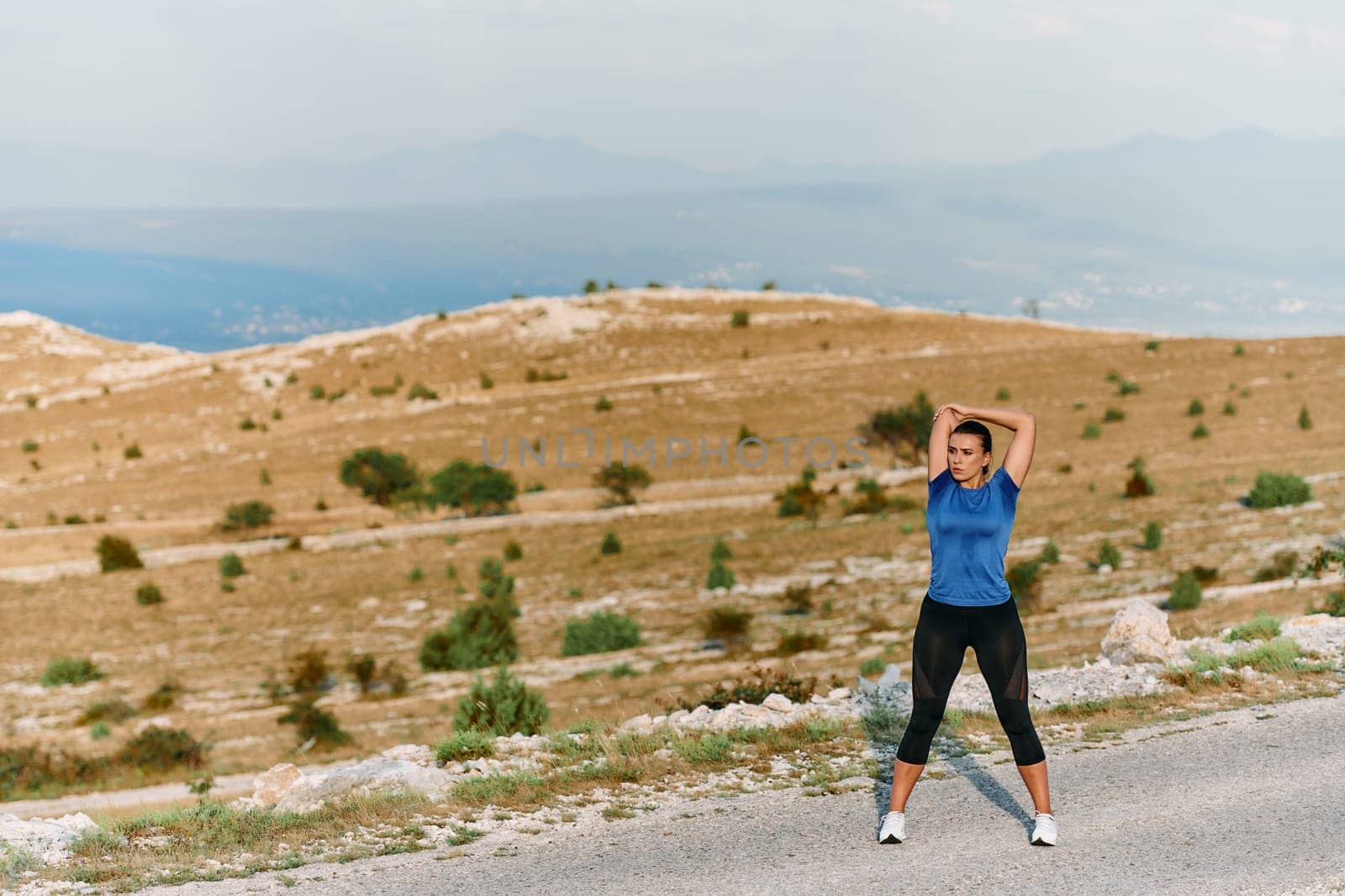 Determined Female Athlete Stretching After an Intense Run Through Rugged Mountain Terrain. by dotshock