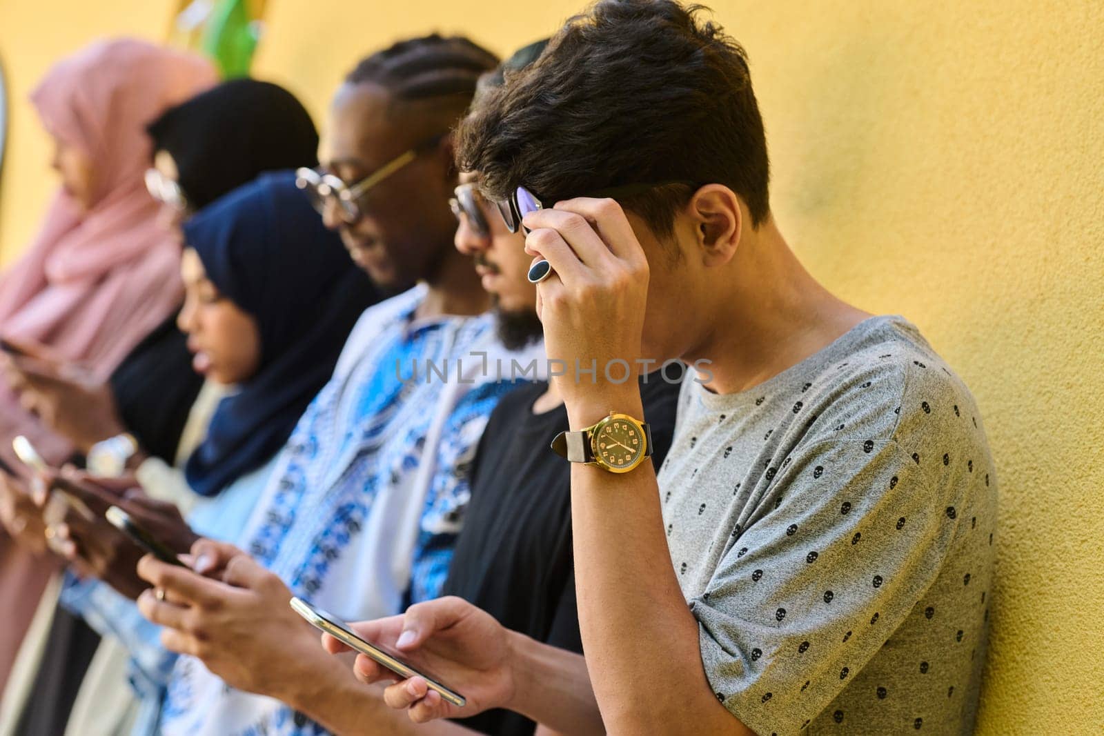 A diverse group of teenagers standing together against a wall, engrossed in their smartphones, showcasing modern connectivity and social interaction.