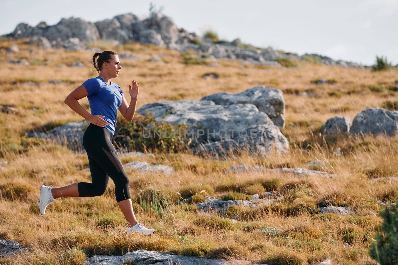 A determined female athlete runs through a forest trail at sunrise, surrounded by breathtaking natural beauty and vibrant greenery.