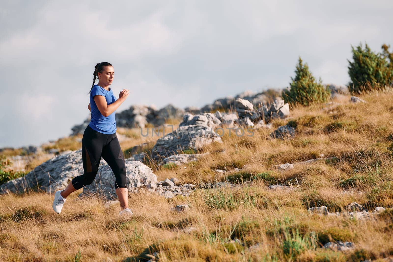 A determined female athlete runs through a forest trail at sunrise, surrounded by breathtaking natural beauty and vibrant greenery.