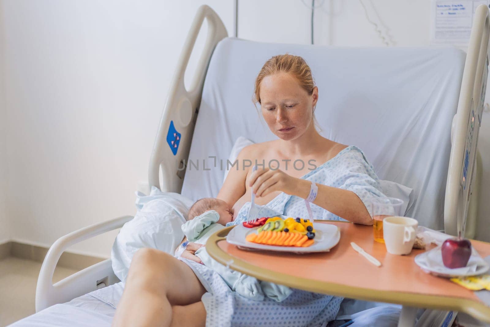 A woman breastfeeds her baby in the hospital while simultaneously having lunch herself. This moment of multitasking illustrates the balance between motherhood and self-care, emphasizing maternal dedication and the nurturing atmosphere of the hospital ward.