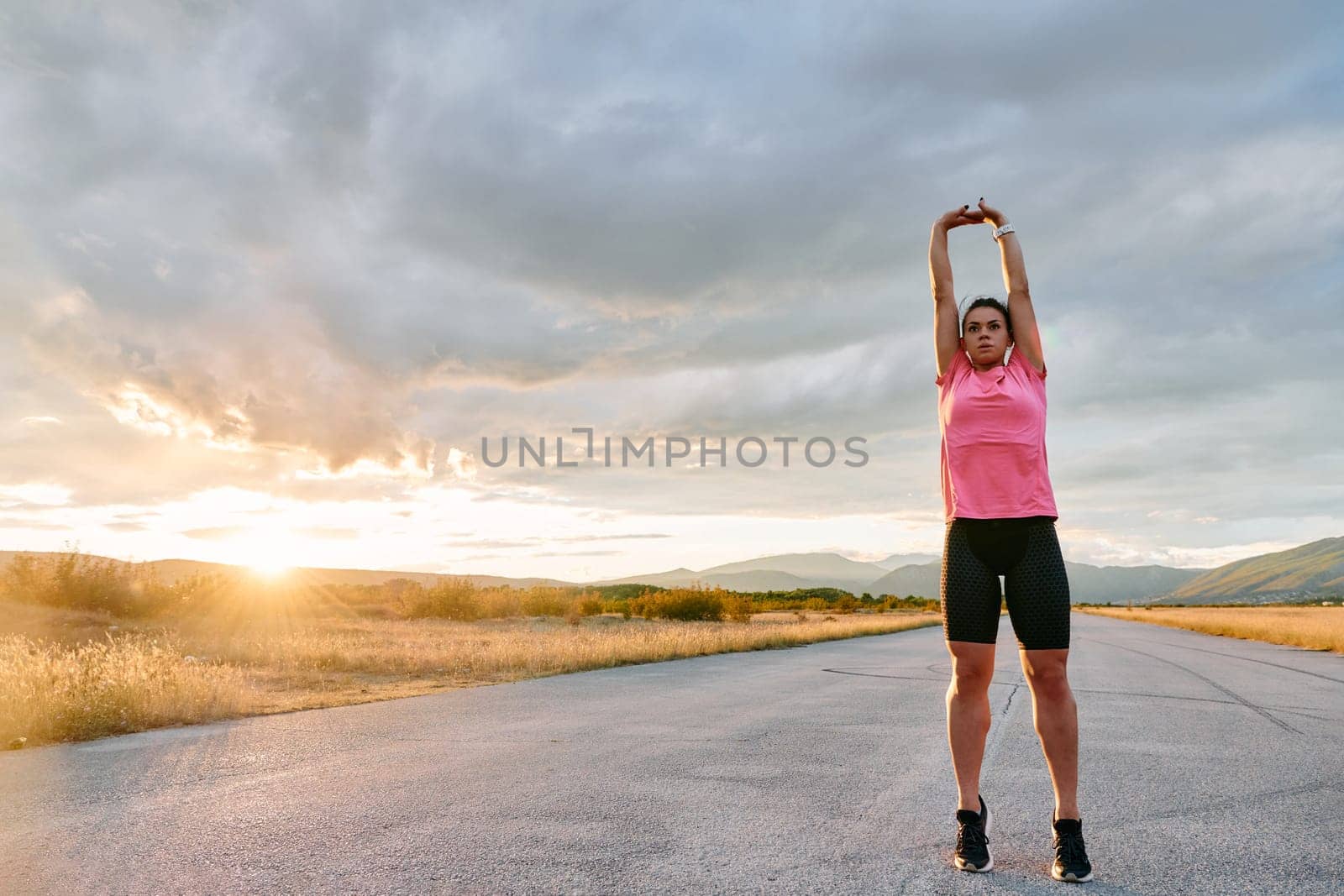 A lone athlete is captured stretching gracefully against the backdrop of a stunning sunset, her silhouette a testament to dedication and resilience after an intense run