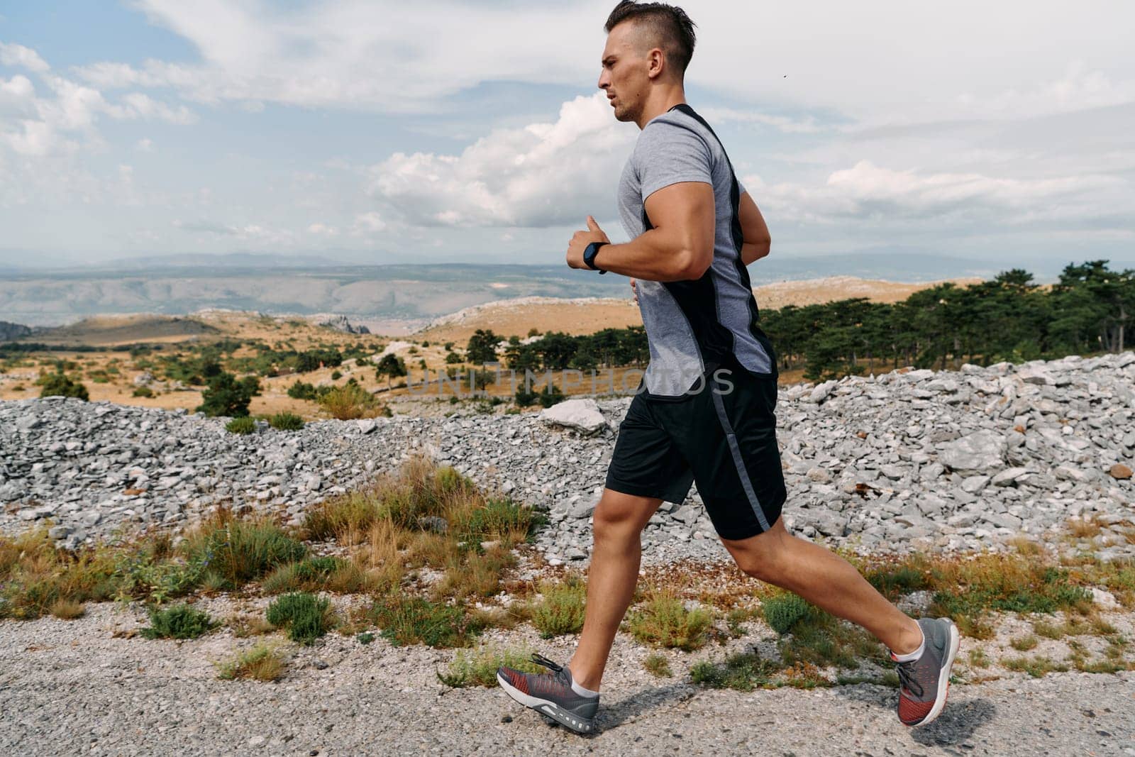 A muscular male athlete runs along a rugged mountain path at sunrise, surrounded by breathtaking rocky landscapes and natural beauty.