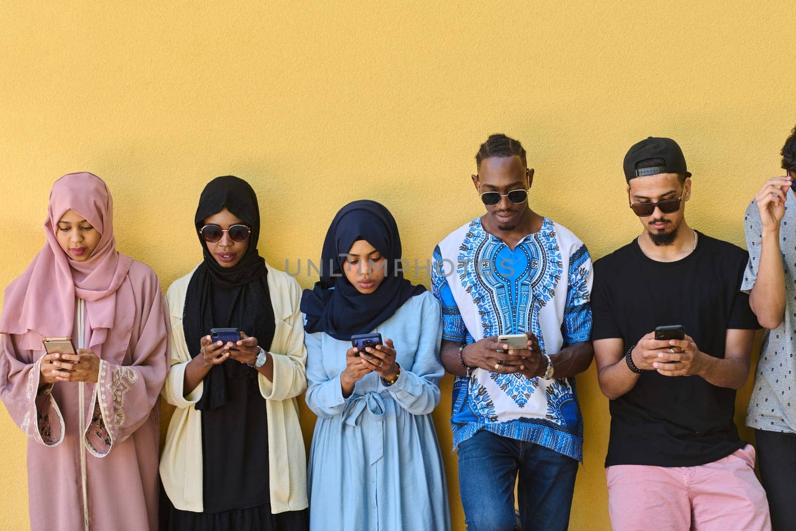 A diverse group of teenagers standing together against a wall, engrossed in their smartphones, showcasing modern connectivity and social interaction.