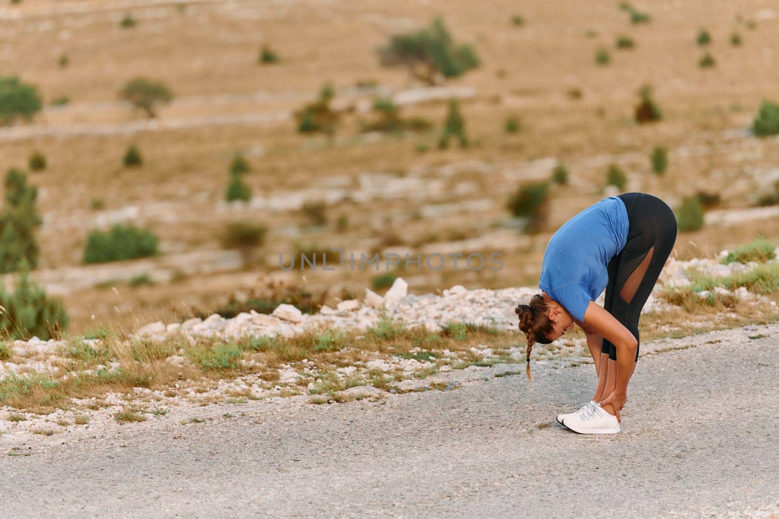 Determined Female Athlete Stretching After an Intense Run Through Rugged Mountain Terrain. by dotshock