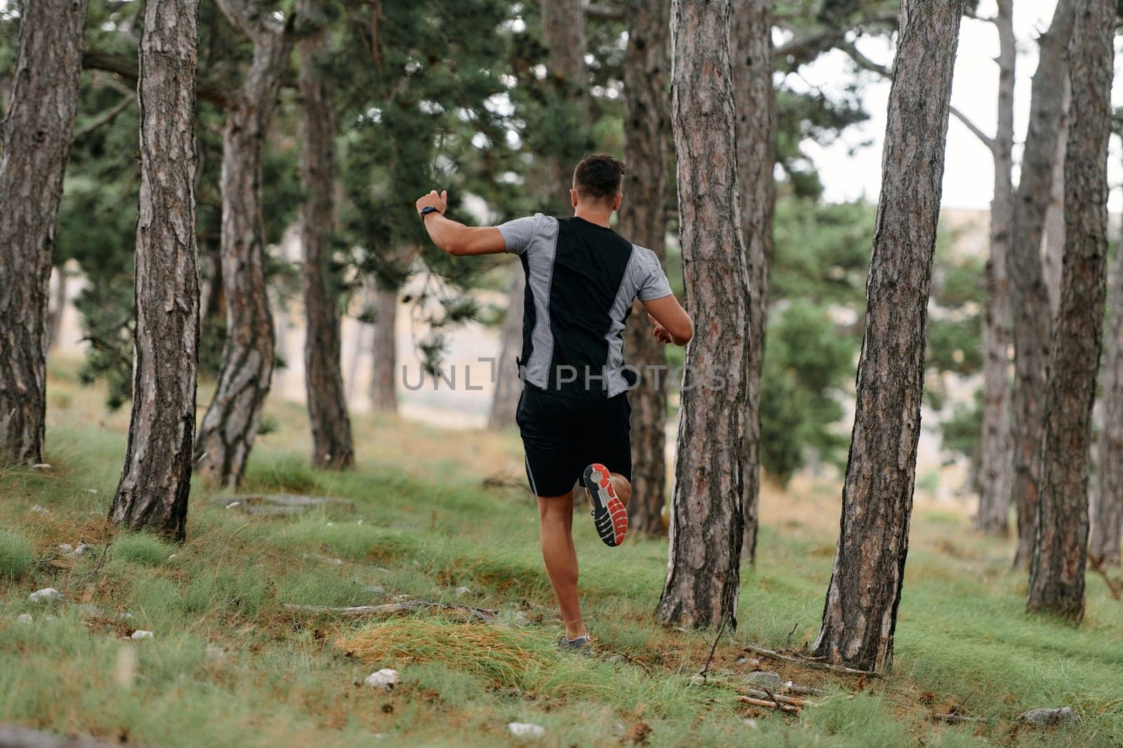 An unwavering man dashes through perilous forest paths, skillfully hurdling over wooden obstacles with determination and agility, epitomizing courage and athleticism