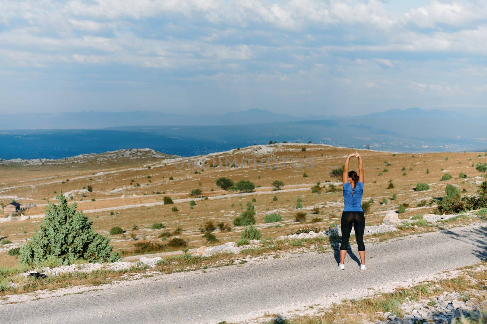 A determined female athlete stretches her muscles after a strenuous run through rugged mountain terrain, surrounded by breathtaking rocky landscapes.