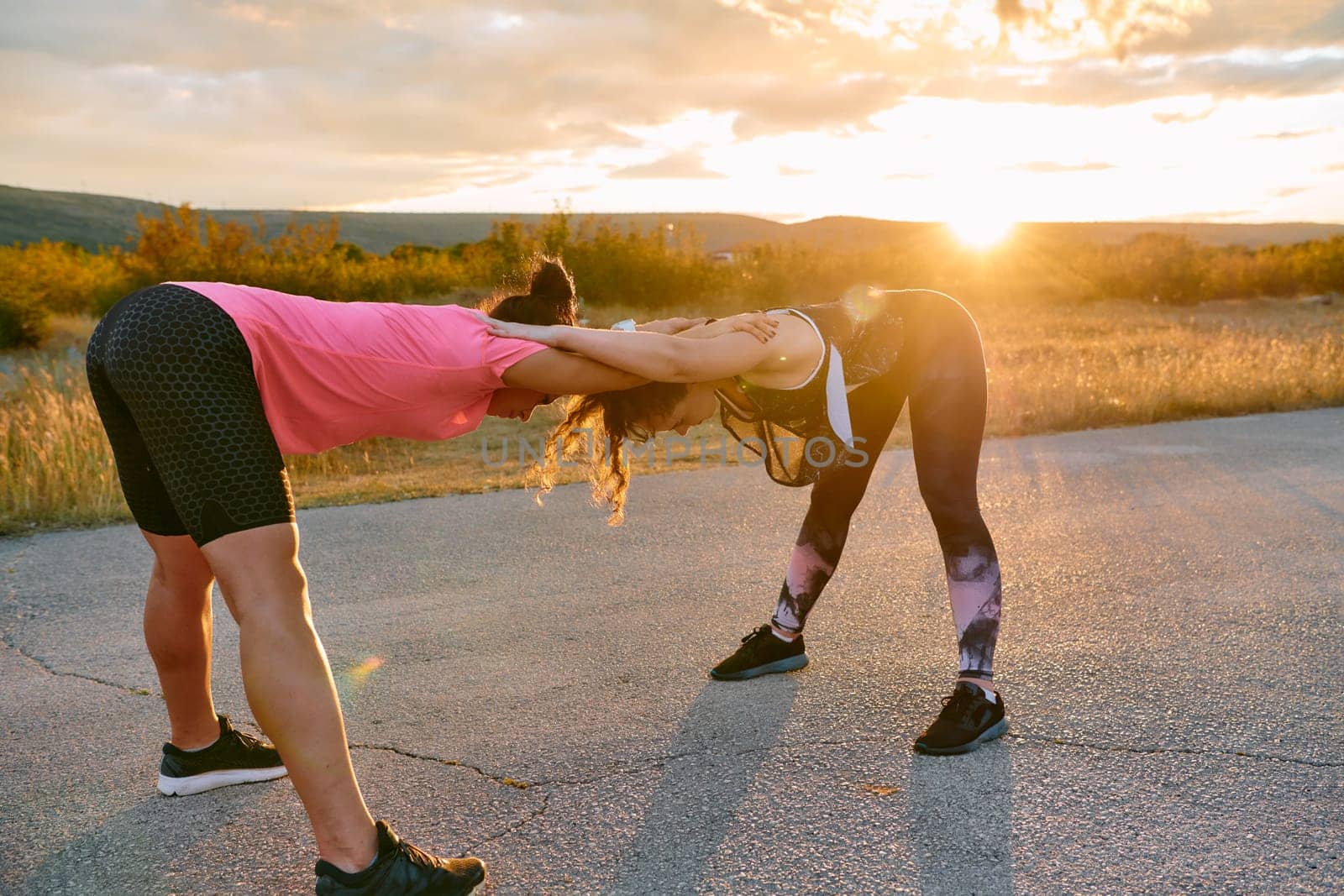 Two Women Athletes Stretching at Sunset in Beautiful Natural Surroundings by dotshock