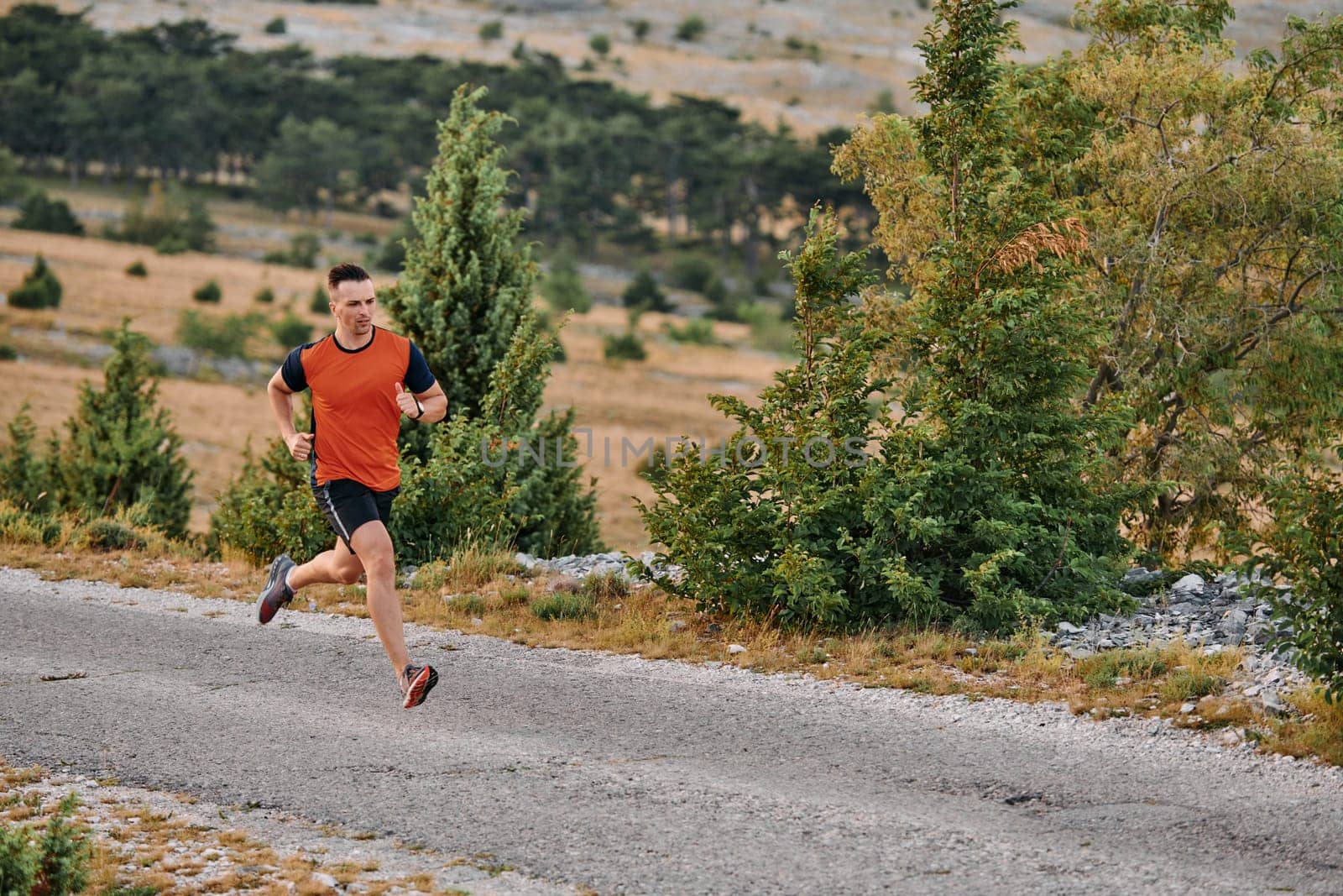 A muscular male athlete runs along a rugged mountain path at sunrise, surrounded by breathtaking rocky landscapes and natural beauty.