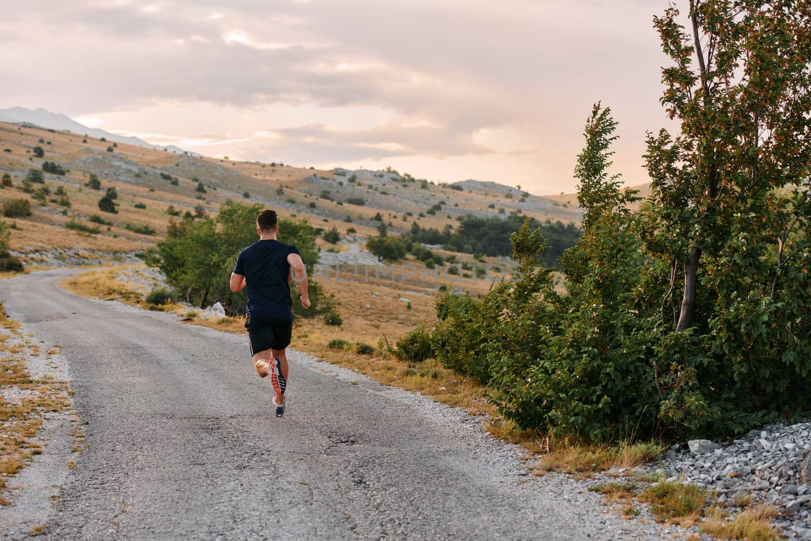 A muscular male athlete runs along a rugged mountain path at sunrise, surrounded by breathtaking rocky landscapes and natural beauty.