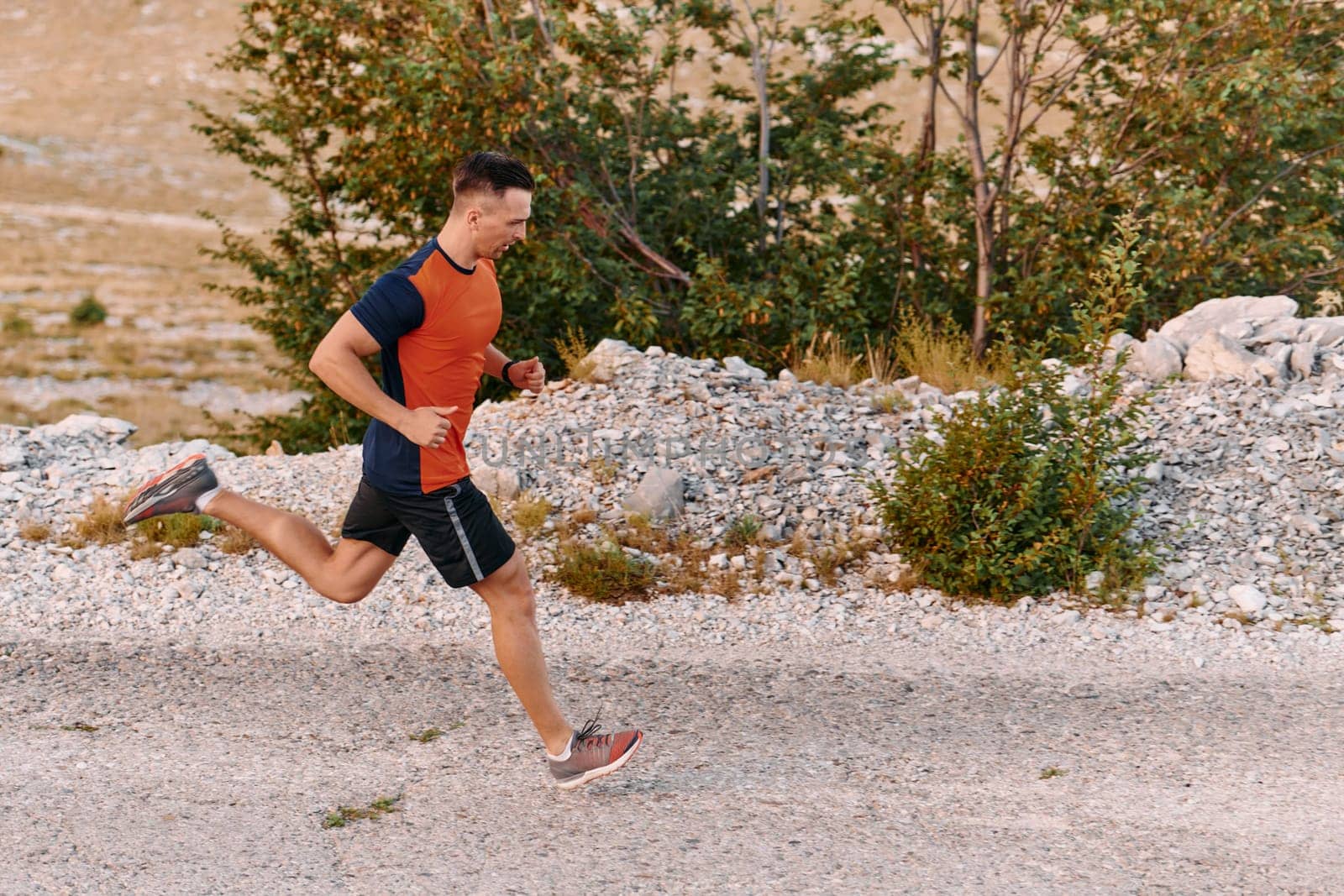 A muscular male athlete runs along a rugged mountain path at sunrise, surrounded by breathtaking rocky landscapes and natural beauty.