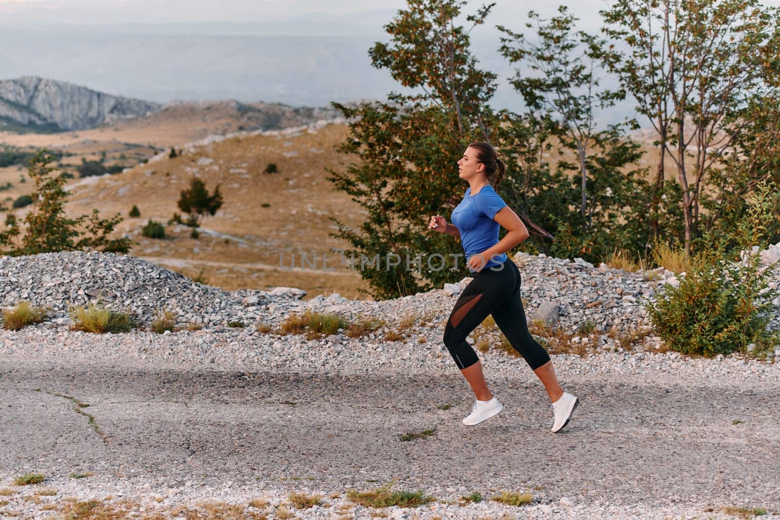 A determined female athlete runs through a forest trail at sunrise, surrounded by breathtaking natural beauty and vibrant greenery.