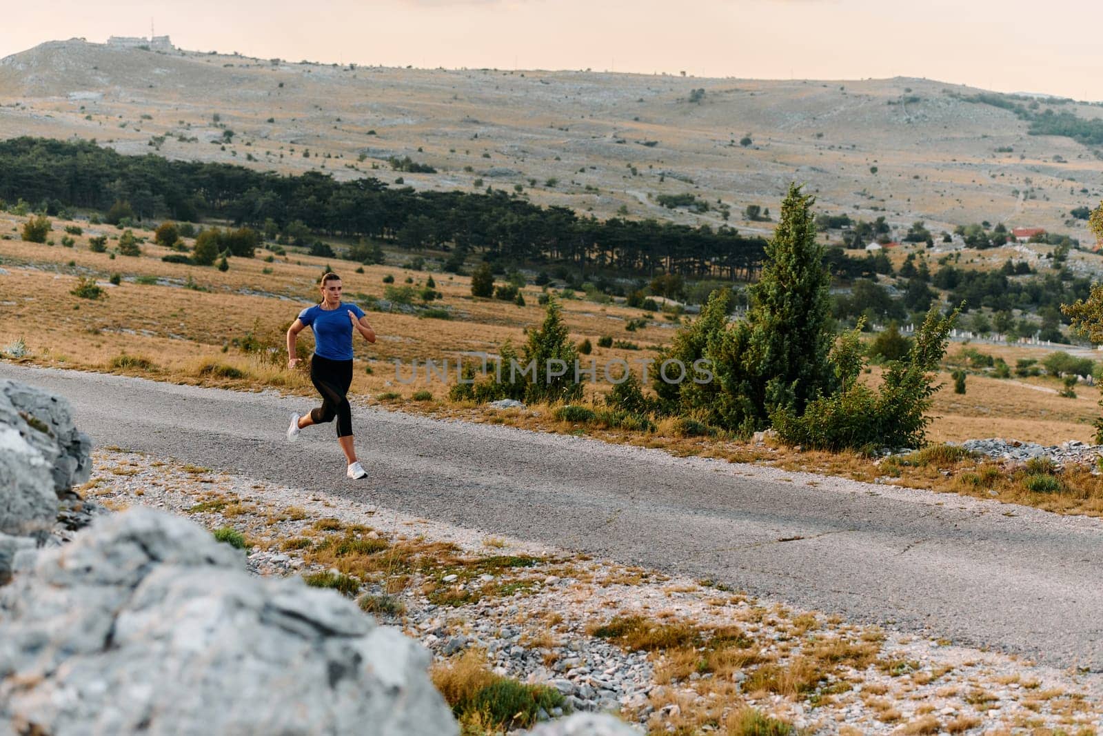 A determined female athlete runs through a forest trail at sunrise, surrounded by breathtaking natural beauty and vibrant greenery.