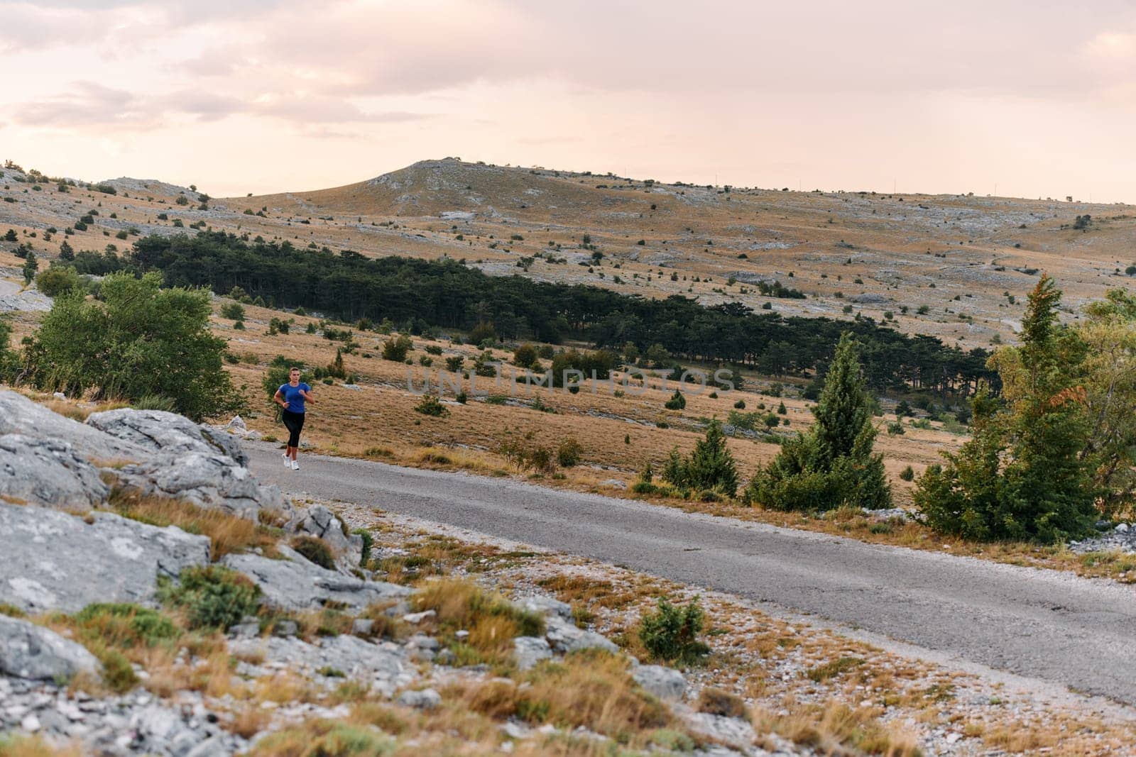 A determined female athlete runs through a forest trail at sunrise, surrounded by breathtaking natural beauty and vibrant greenery.