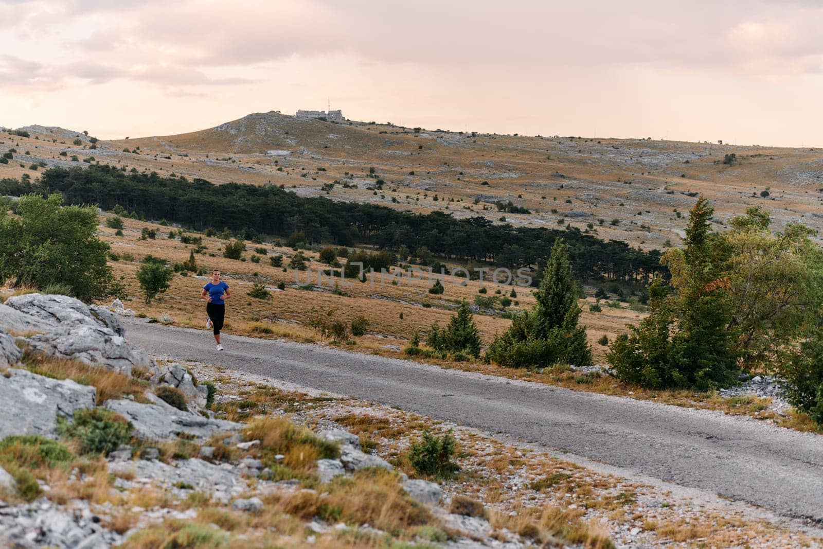 A determined female athlete runs through a forest trail at sunrise, surrounded by breathtaking natural beauty and vibrant greenery.