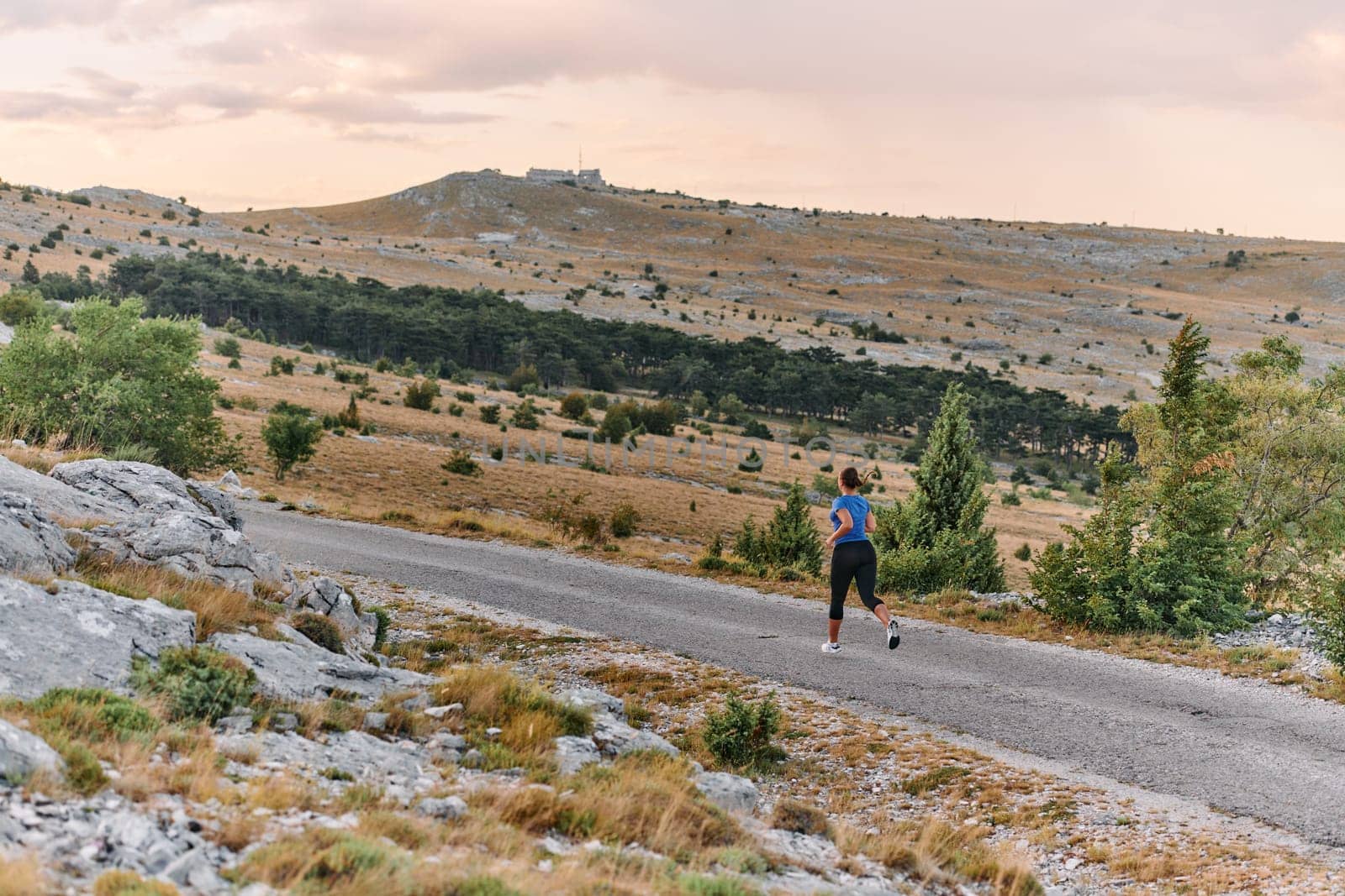 A determined female athlete runs through a forest trail at sunrise, surrounded by breathtaking natural beauty and vibrant greenery.