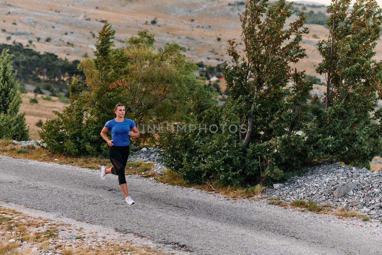 A determined female athlete runs through a forest trail at sunrise, surrounded by breathtaking natural beauty and vibrant greenery.