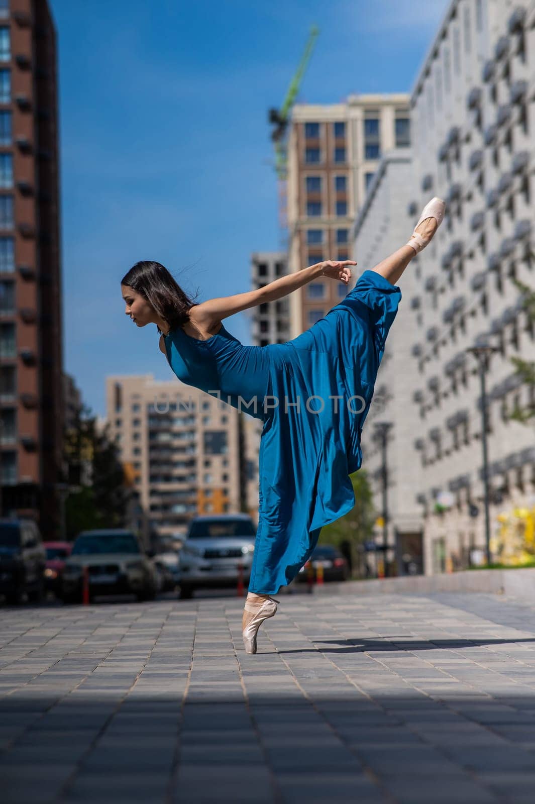 Beautiful Asian ballerina in blue dress posing in splits outdoors. Urban landscape. Vertical photo. by mrwed54