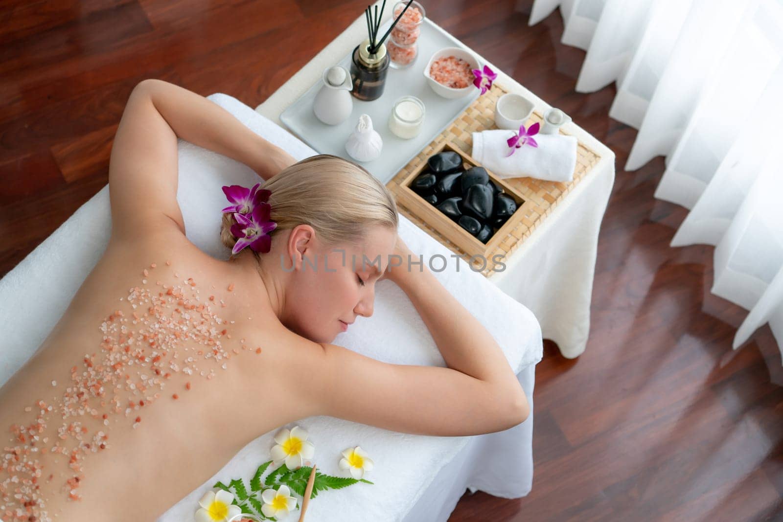 Panorama top view woman customer having exfoliation treatment in luxury spa salon with warmth candle light ambient. Salt scrub beauty treatment in health spa body scrub. Quiescent