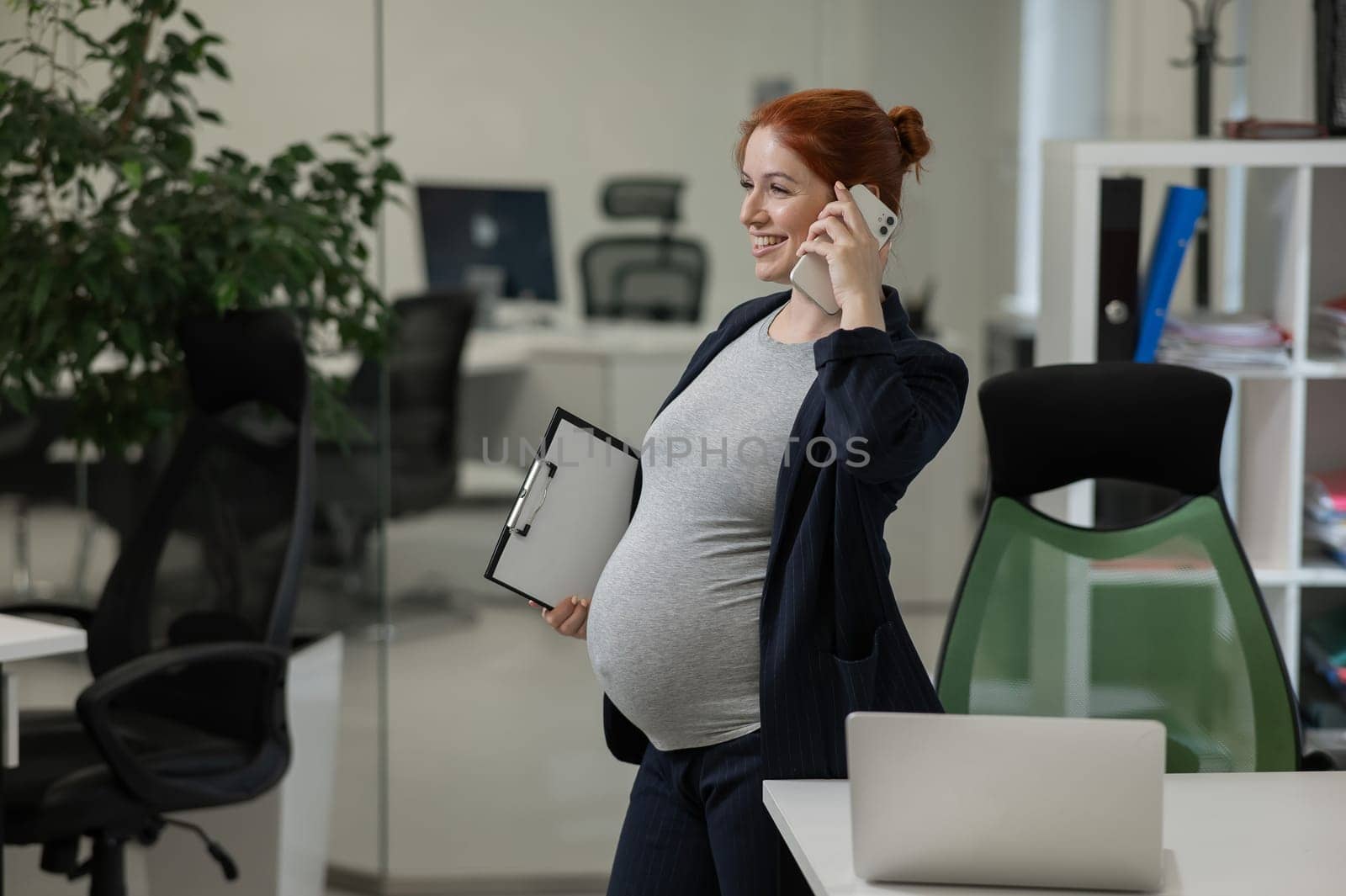 Pregnant woman using mobile phone and holding paper tablet in office. by mrwed54