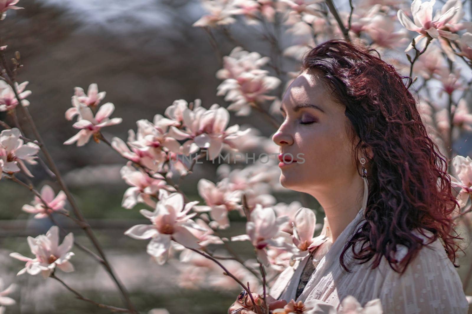 Magnolia park woman. Stylish woman in a hat stands near the magnolia bush in the park. Dressed in white corset pants and posing for the camera. by Matiunina