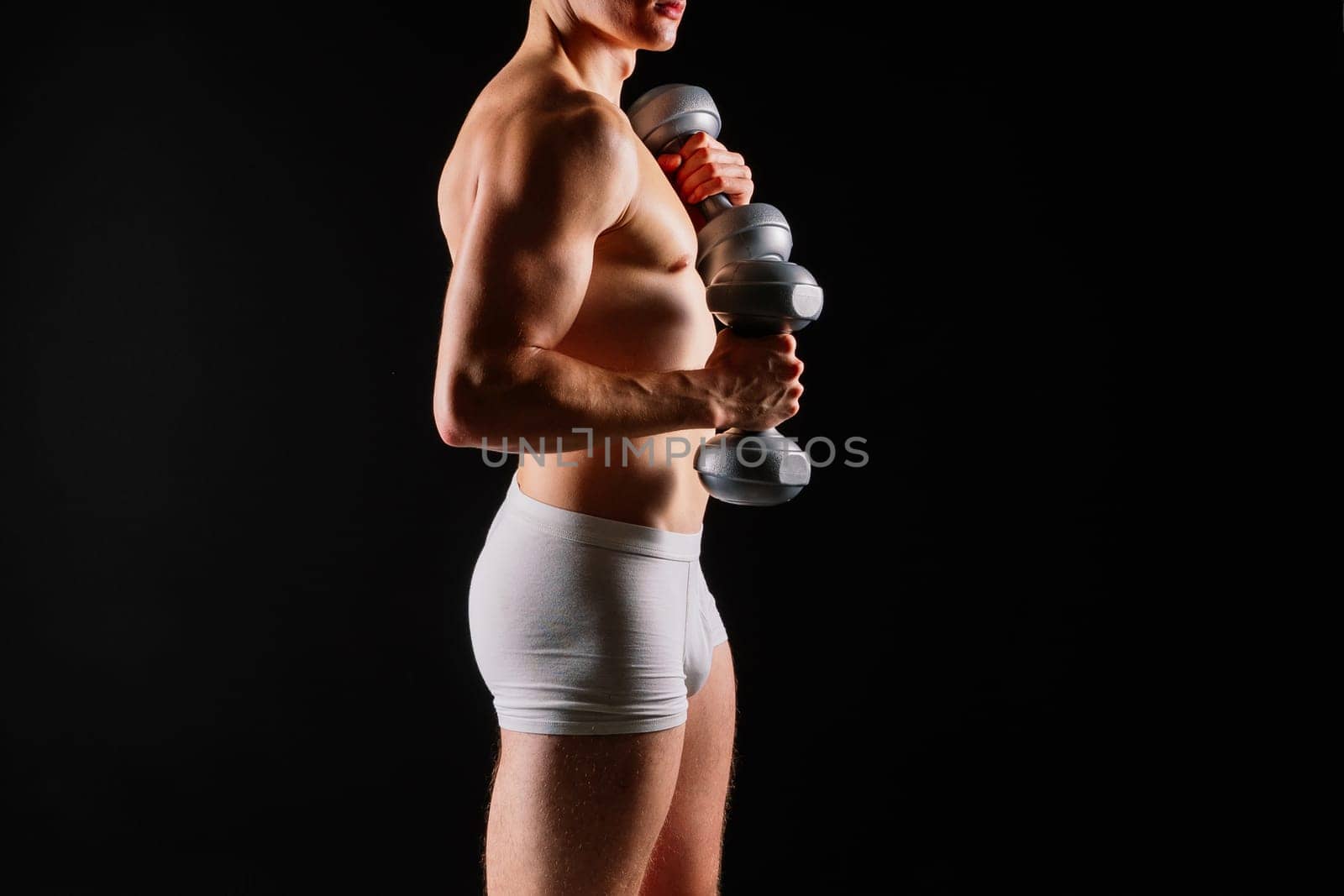 Shirtless bodybuilder holding a dumbell and showing his muscular arms.