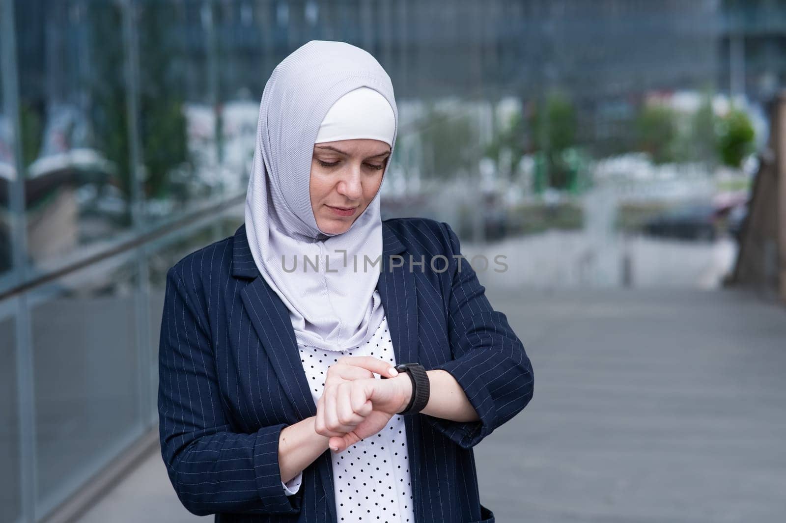 Business woman in hijab and suit uses smart watch outdoors. by mrwed54