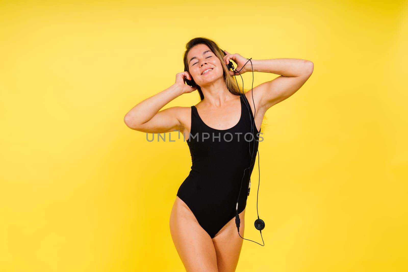 Caucasian Woman in Black Bodysuit Listening to Music in Headphones On Yellow Background. by Zelenin