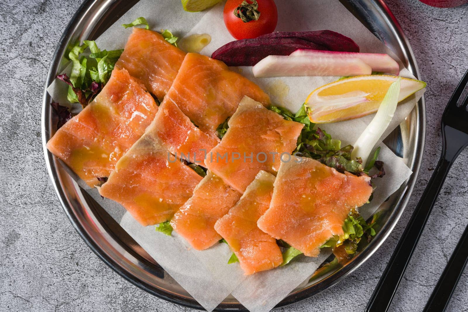 Smoked salmon with greens under it on a stone table