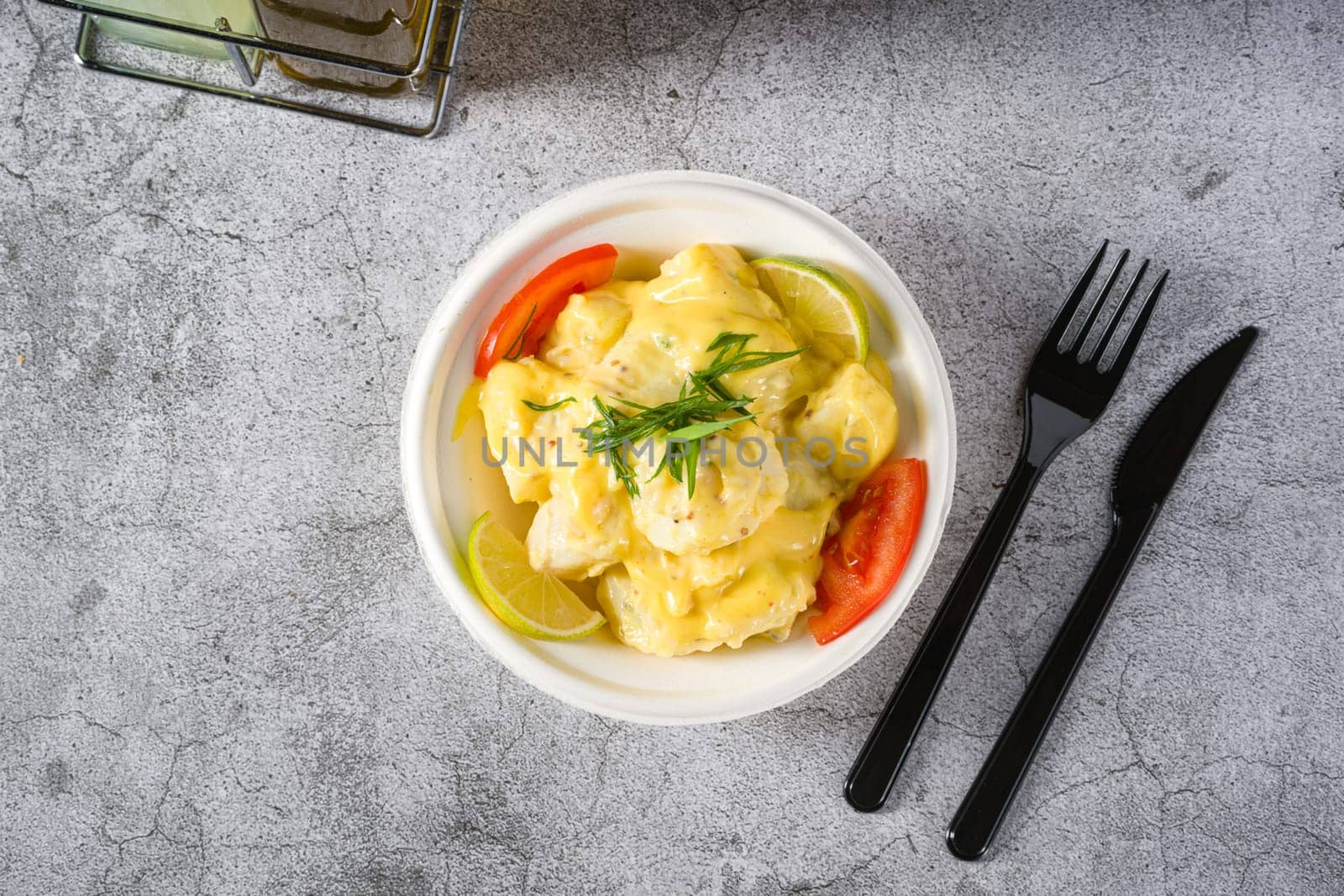 Potato salad with tomatoes and lemon on gray stone table by Sonat