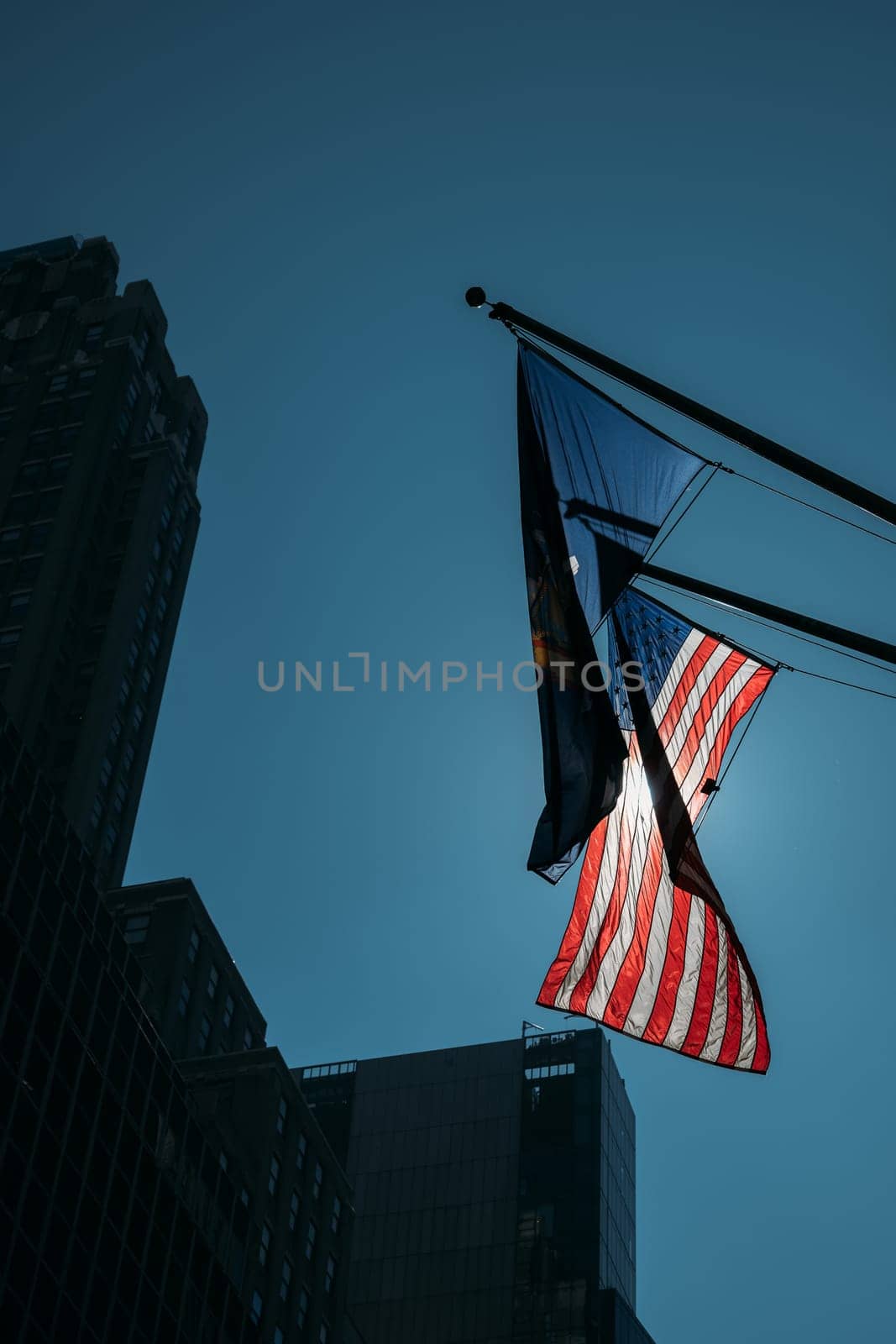 A view of an American flag waving in the wind against a backdrop of New York City's tall buildings on a clear day.