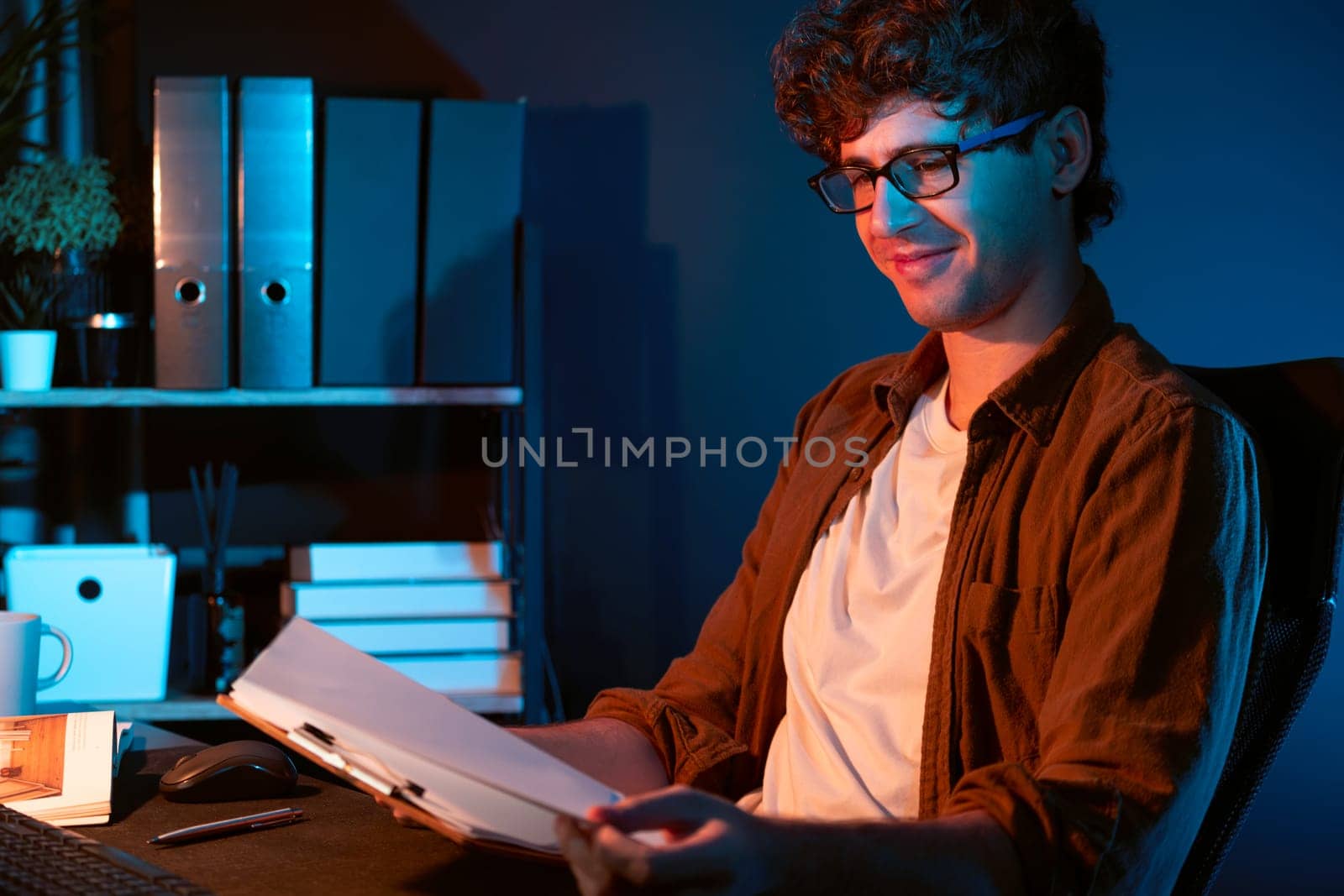 Young businessman reading design thinking on paper for new project surround work desk at neon light modern office. Thinking new next job sketching on notebook before sending present via email. Gusher.