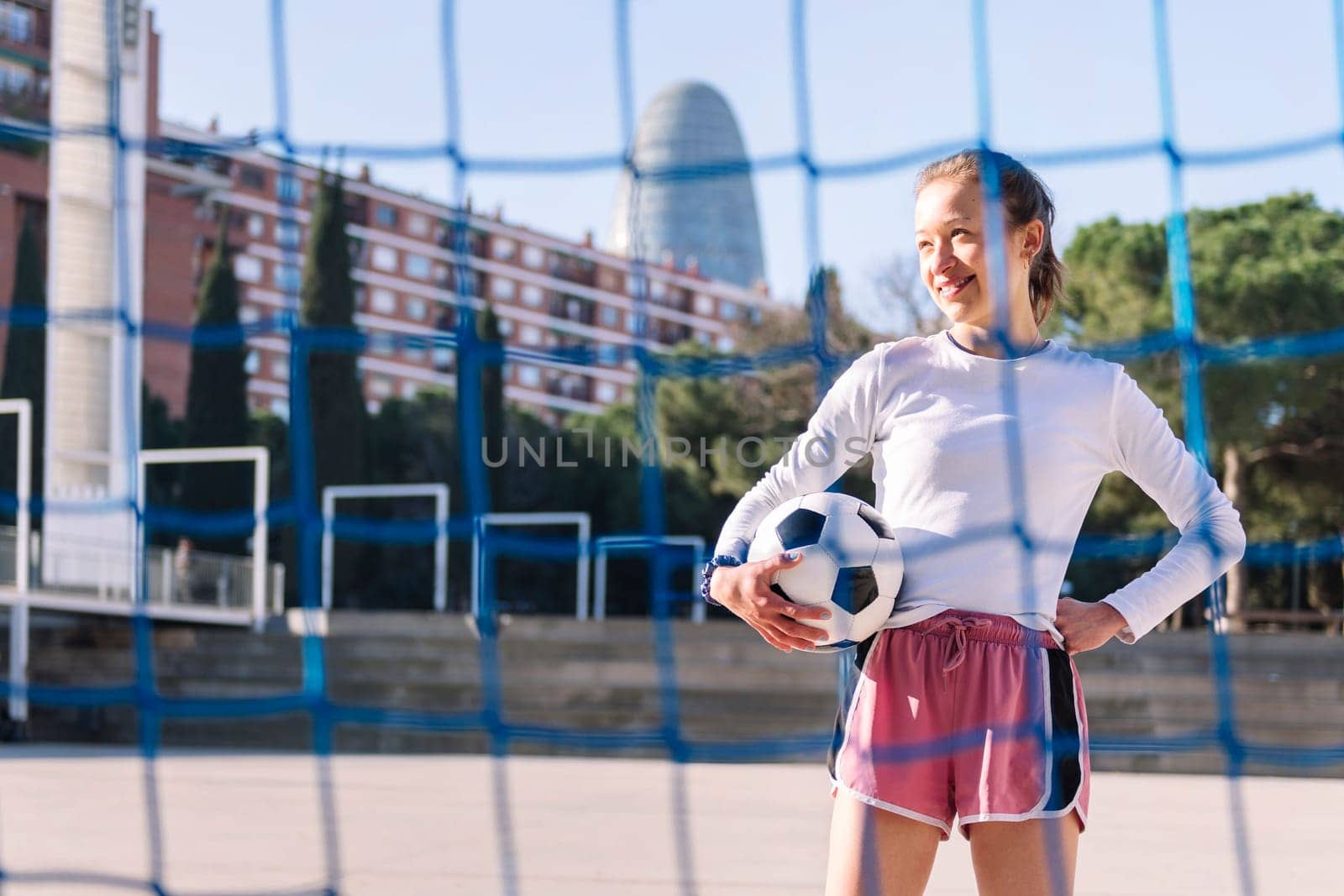 smiling caucasian female football player holding a soccer ball on an urban court, concept of sport and active lifestyle, copy space for text