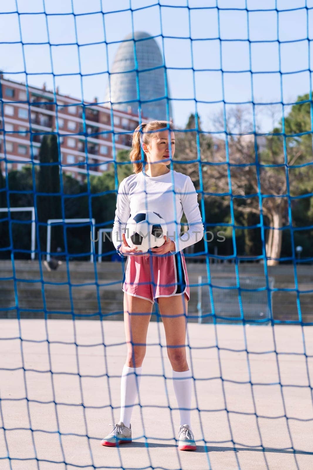 caucasian female football player standing holding a soccer ball on an urban court, concept of sport and active lifestyle