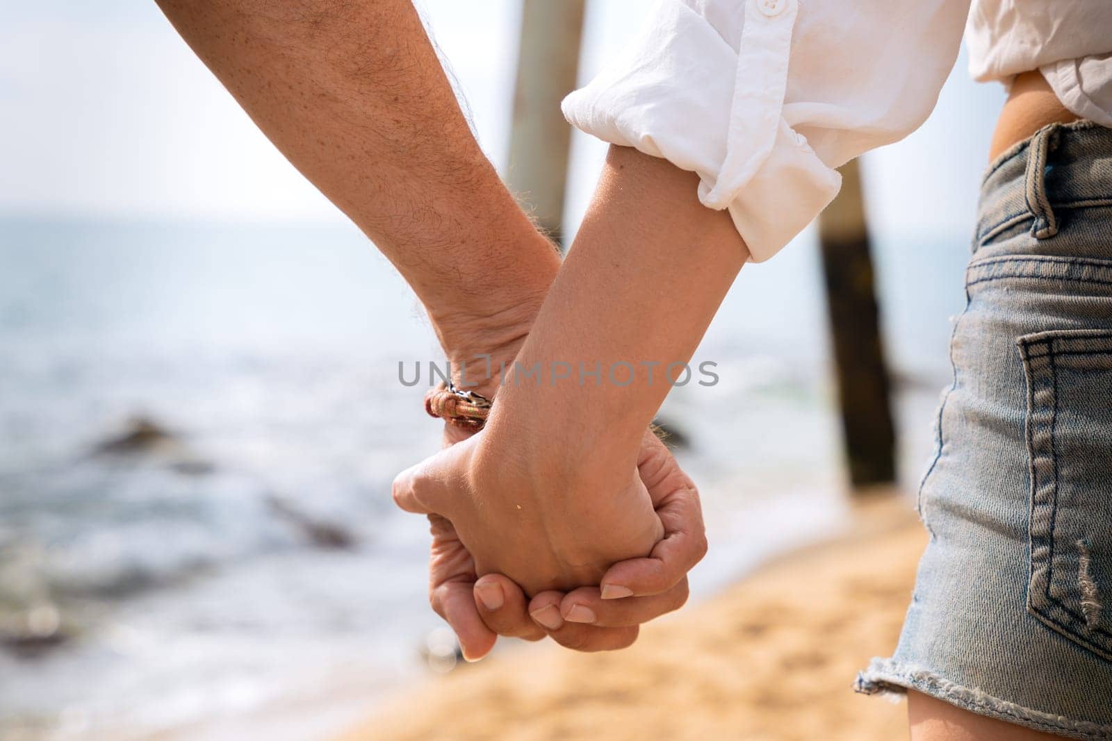 Happy couple in love holding hands and looking at each other on the seashore. A man and a woman are standing on the sand near the ocean. Vows and promises on the seashore.